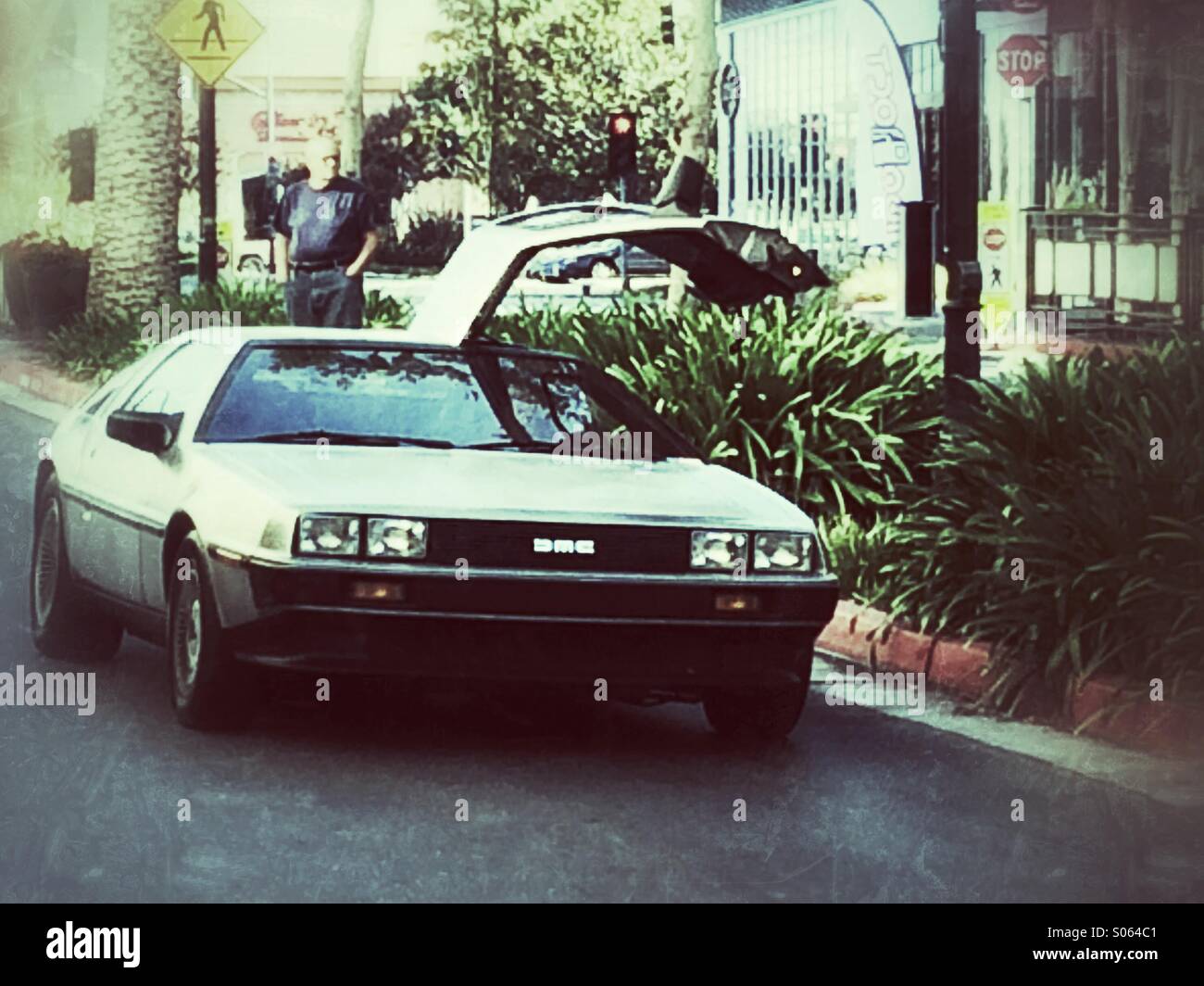 Man drives his 1981 DeLorean DMC 12 down the street with his car door open. - Smartphone Captured Stock Image