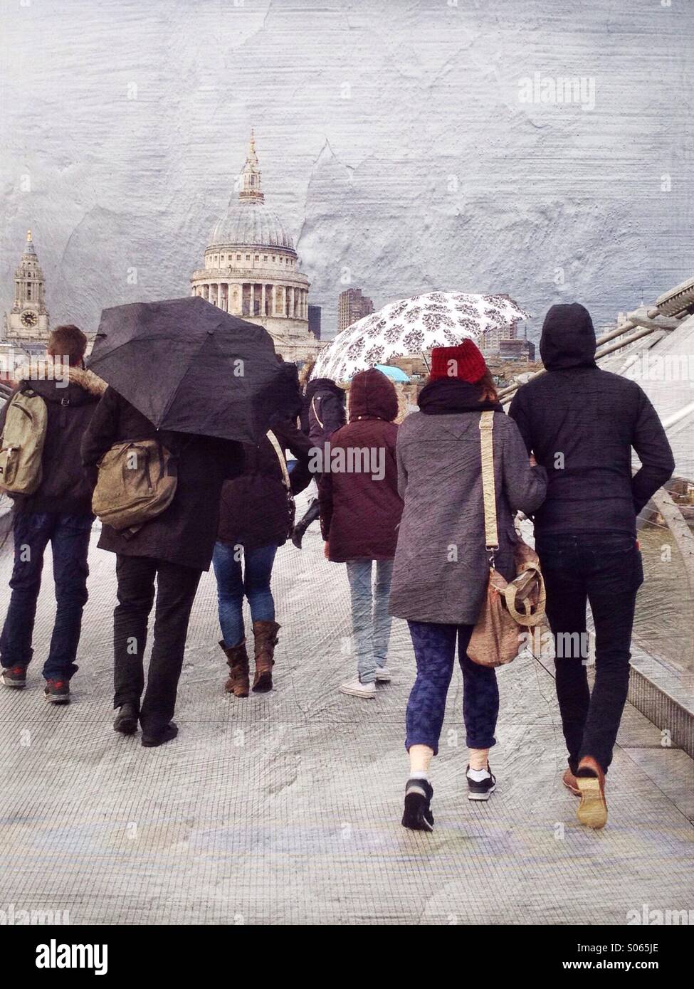 A rainy day in London Town - tourists cross the Millennium Bridge towards St Paul's Cathedral with umbrellas to keep off the English weather Stock Photo