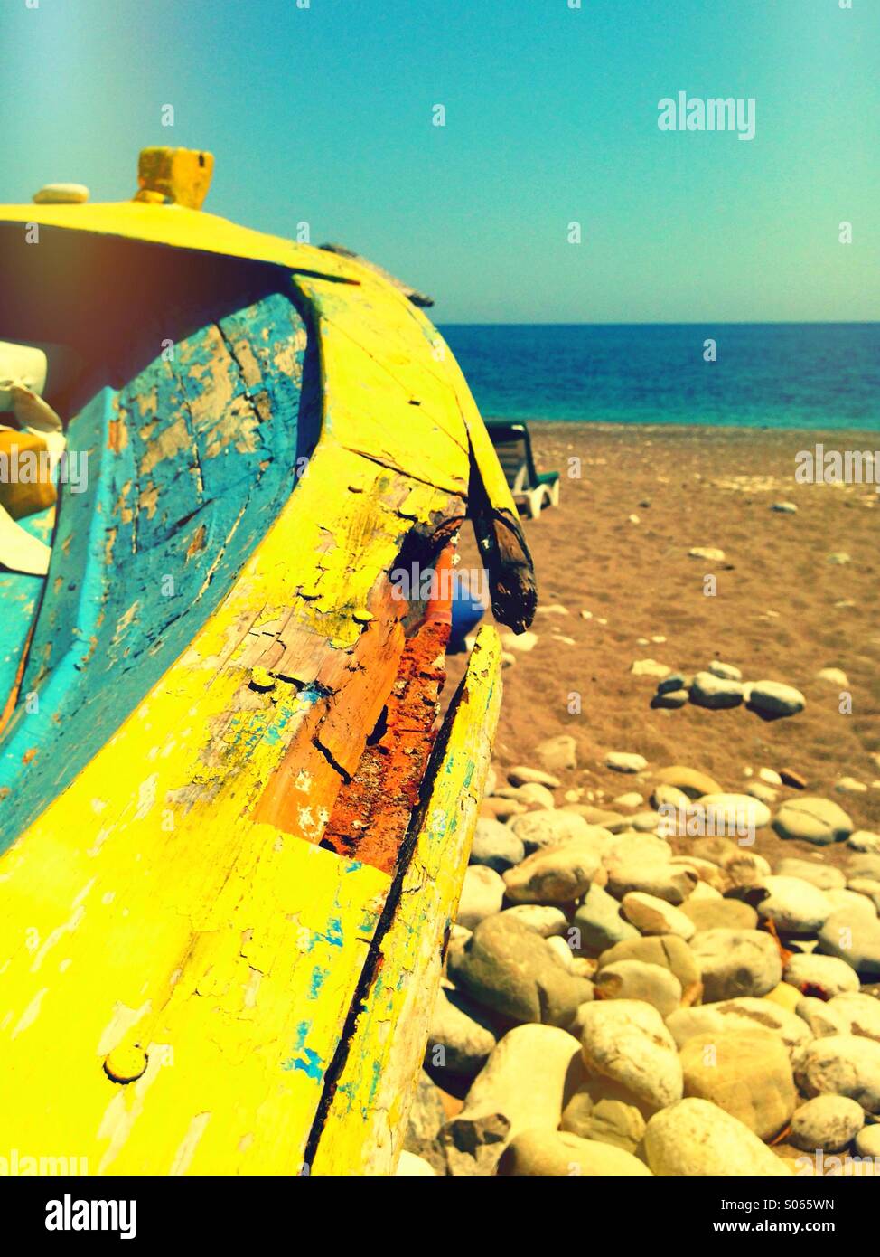 Vintage painted boat on a sand and pebble Mediterranean beach. Stock Photo