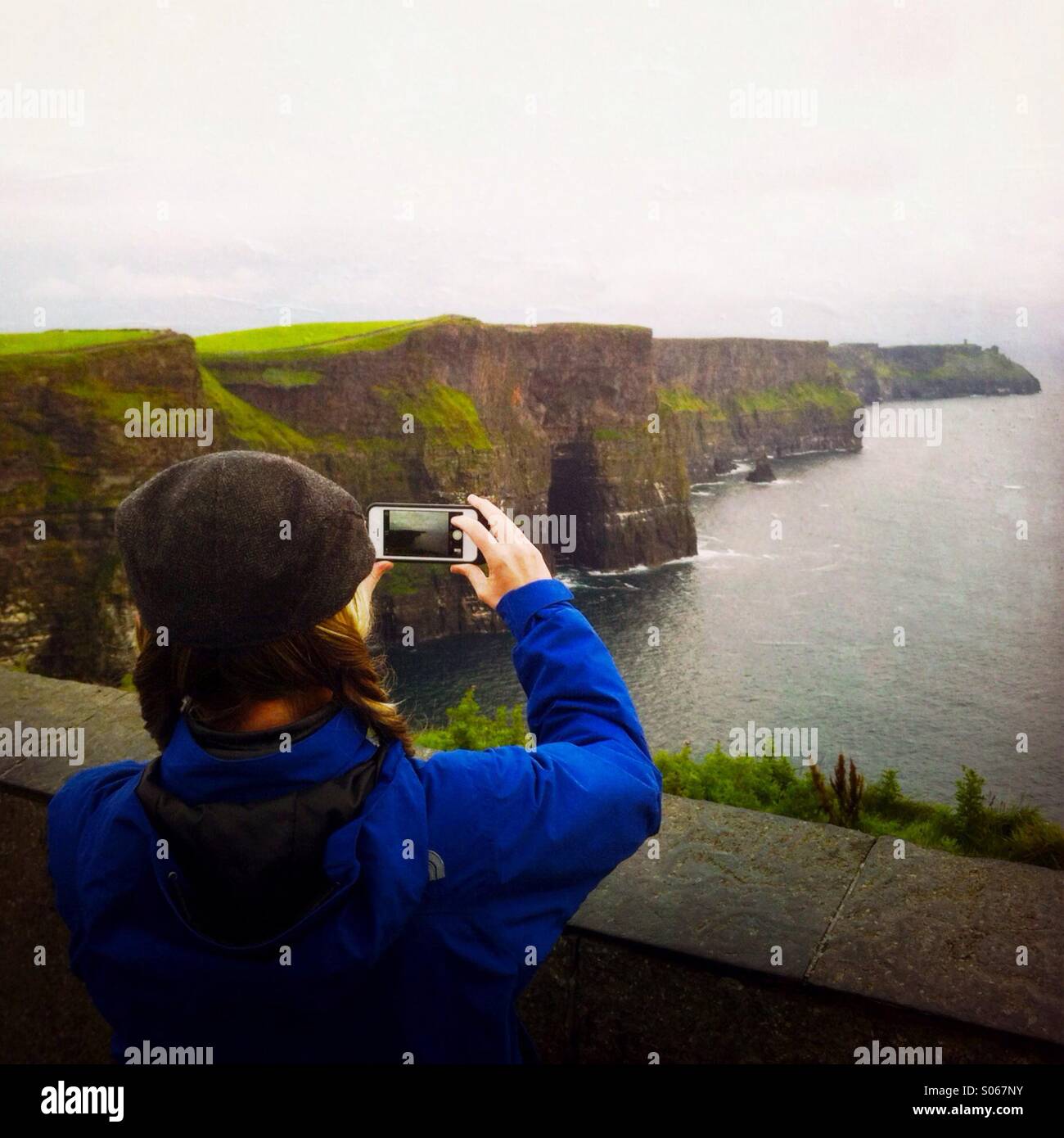 A woman taking a photo of the cliffs of moher. County Clare, Ireland  Europe. - Smartphone Captured Stock Image