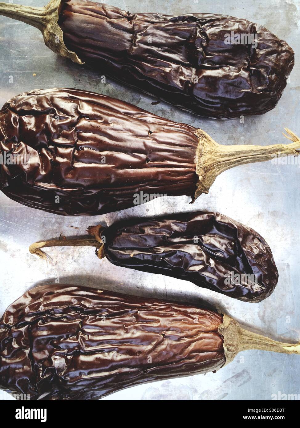 Grilled eggplant (also known as aubergine) on a baking tray after being cooked whole. Stock Photo
