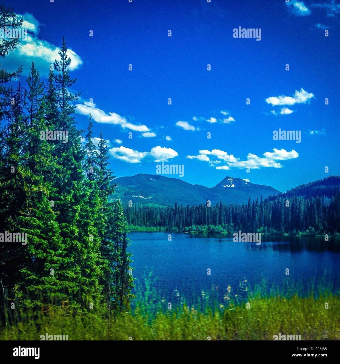 Blue alpine lake surrounded by mountains and trees. - Smartphone Captured Stock Image