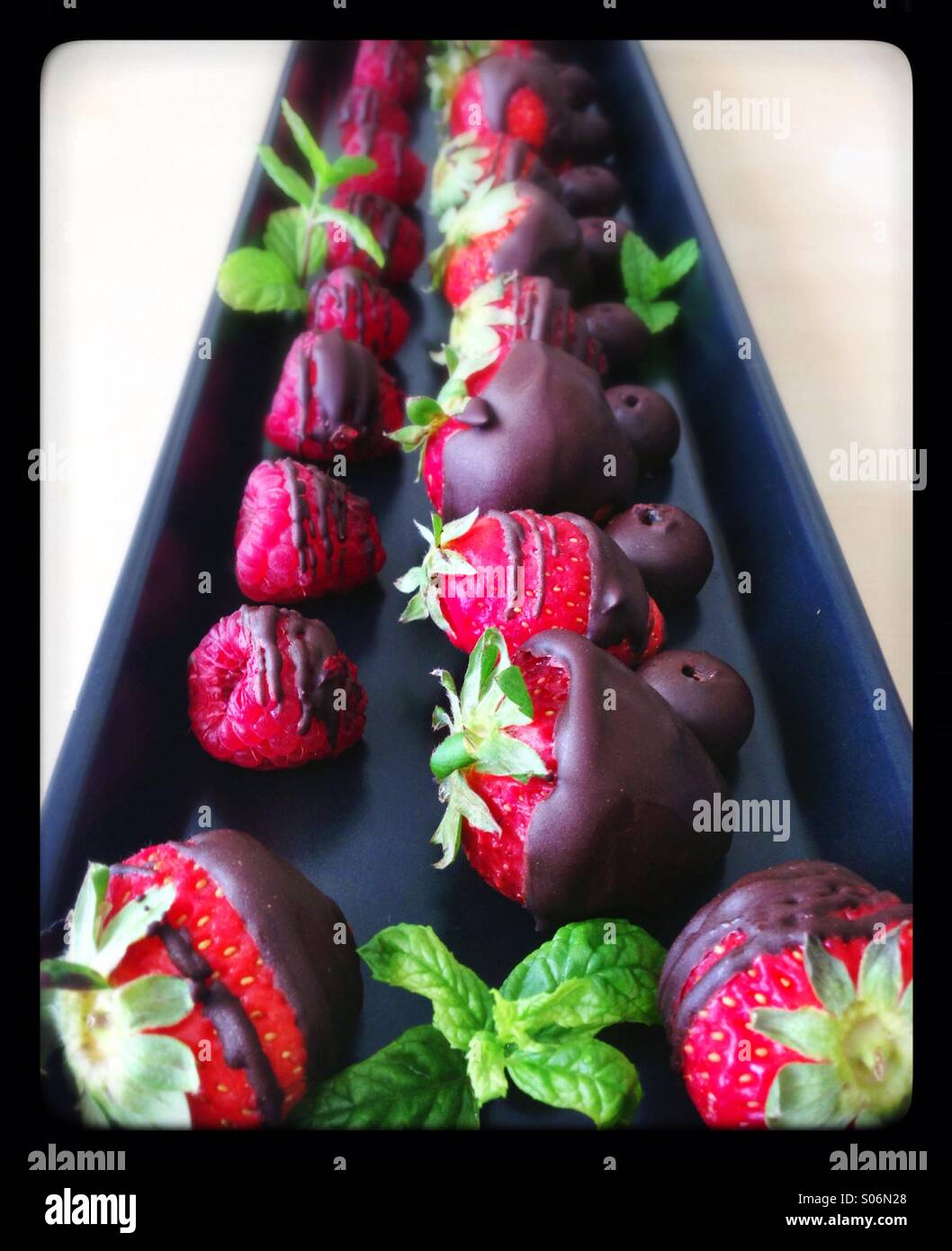 Rectangular black plate of chocolate covered red fruits - Smartphone Captured Stock Image