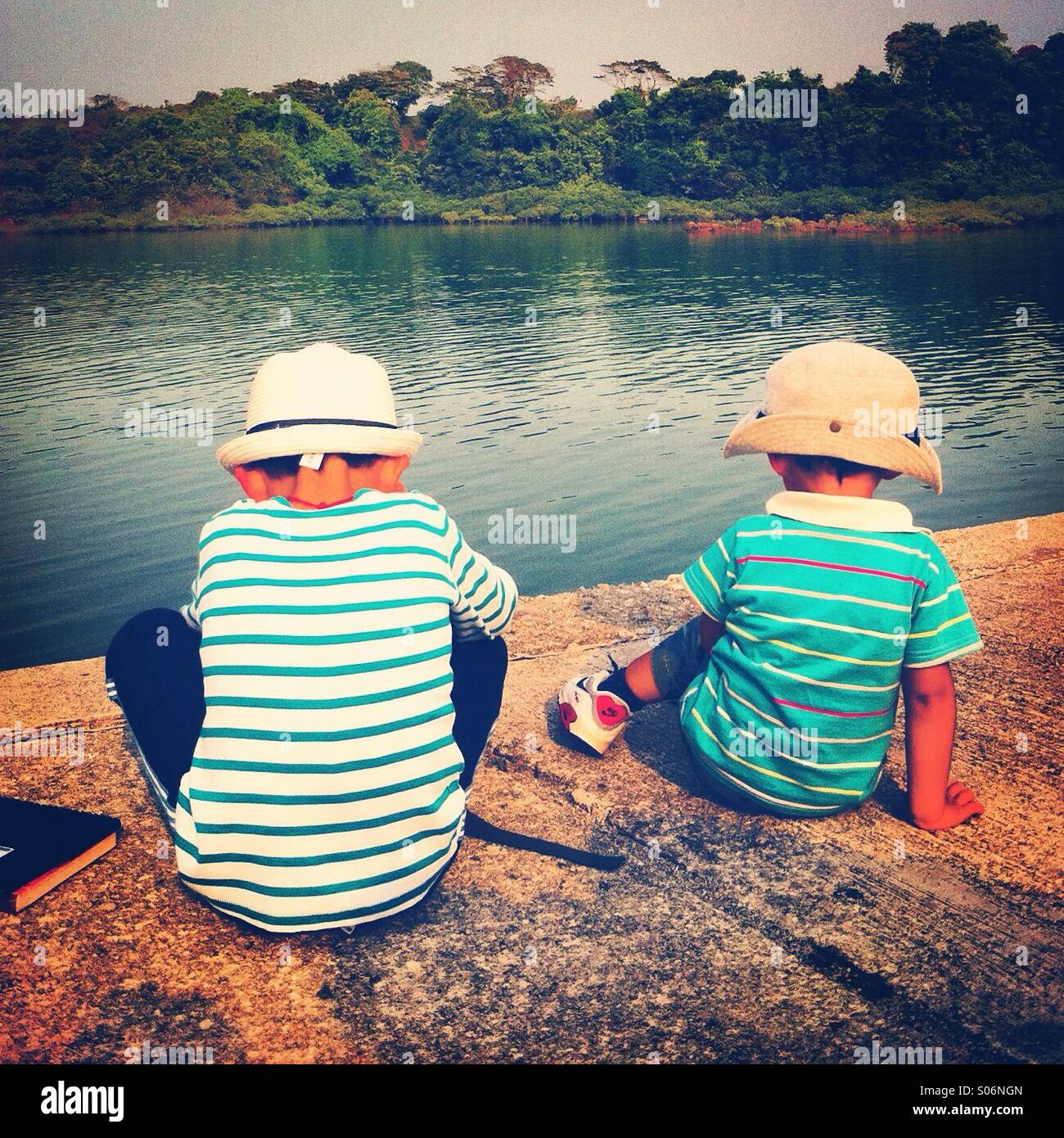 Two kids, view from the back, sitting doan on floor near the water Stock Photo