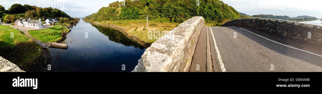 Panoramic shot of the Clachan Bridge or Bridge over the Atlantic at Seil Island near Easdale and Oban in Scotland showing the roadway of the bridge and the nearby white cottages alongside the sea. Stock Photo