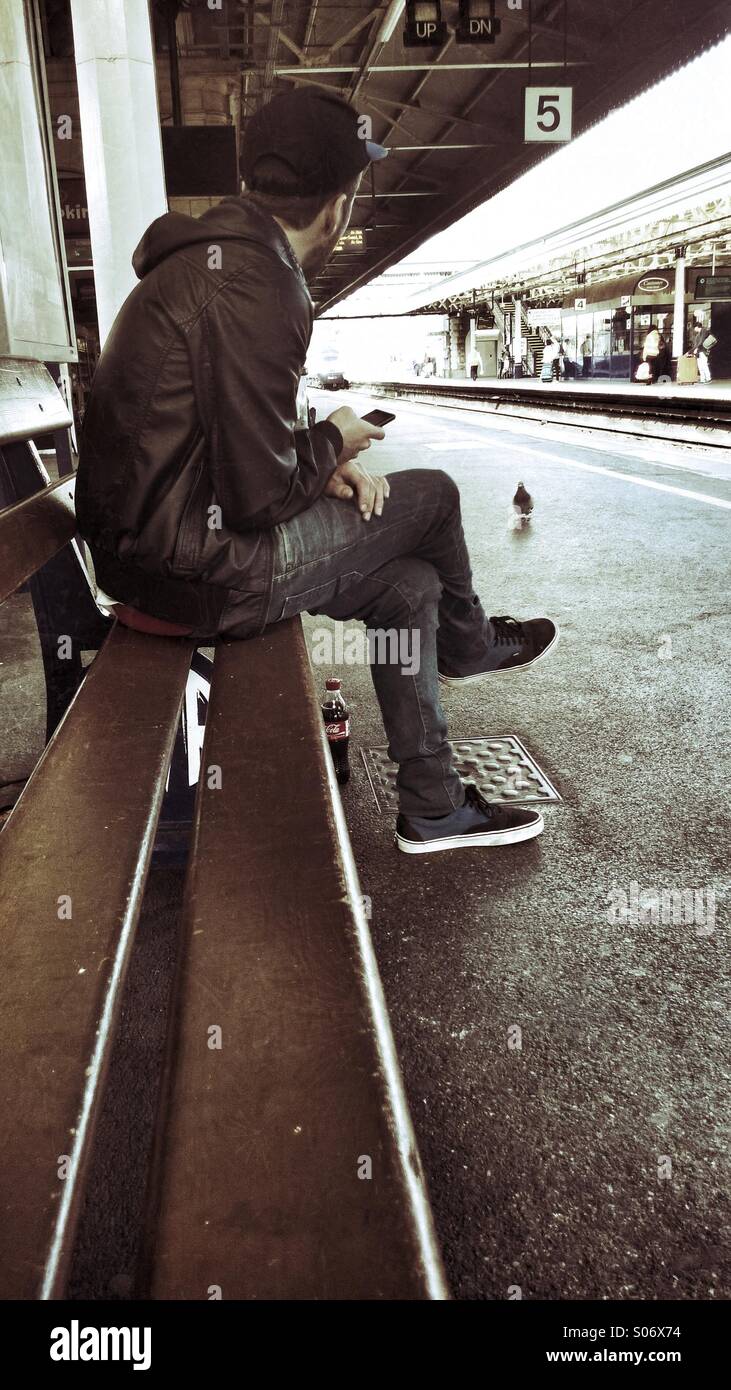 Young man using smartphone while waiting for a train. - Smartphone Captured Stock Image