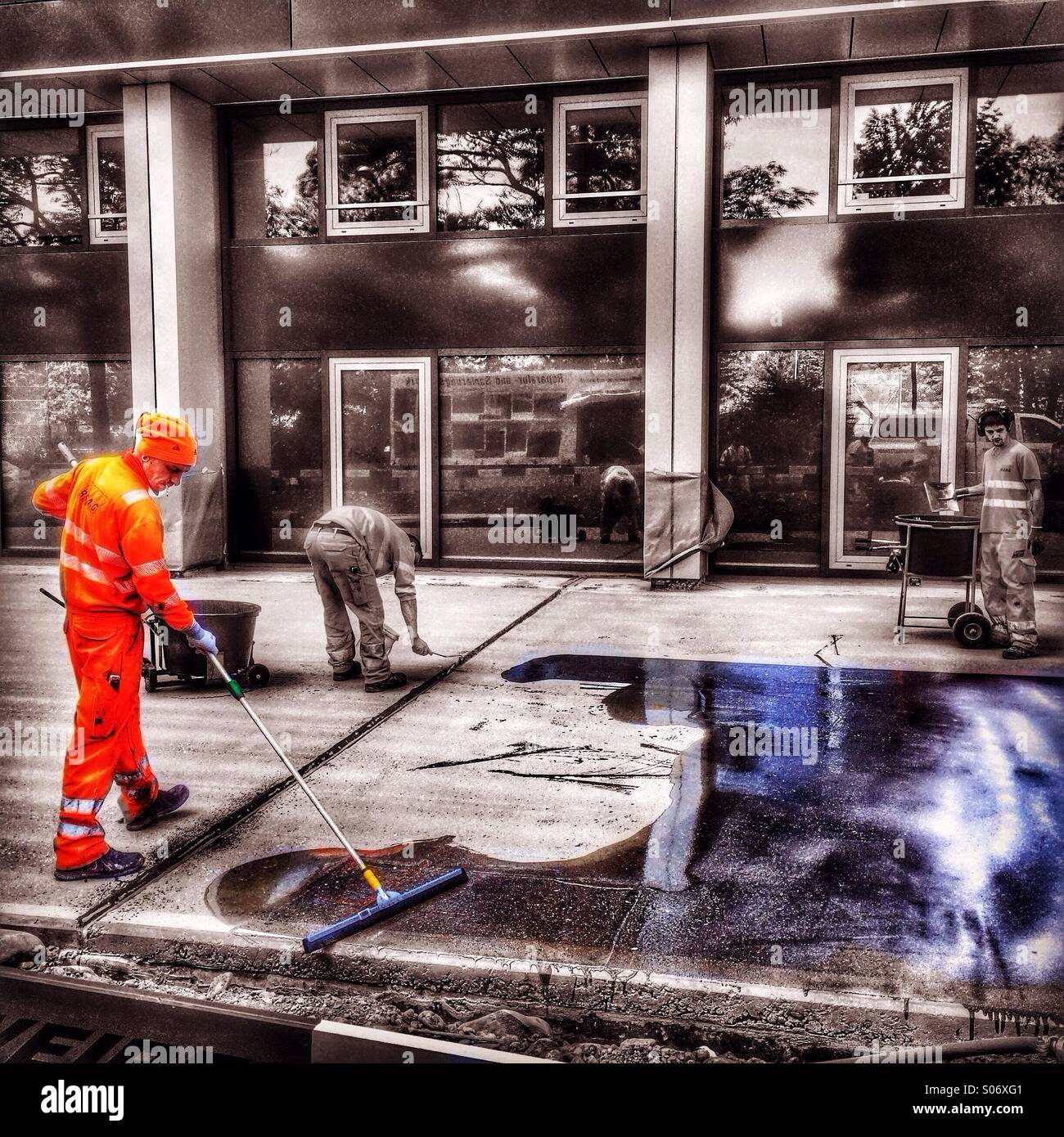 Workman in orange clothes paints colour onto the ground - Smartphone Captured Stock Image