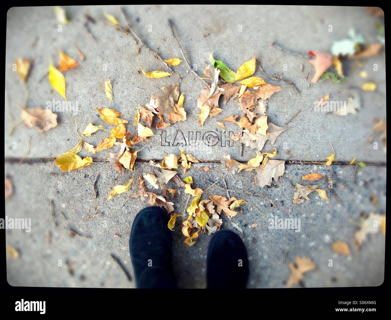A person's feet standing next to the word 'laugh' carved into a sidewalk. Stock Photo