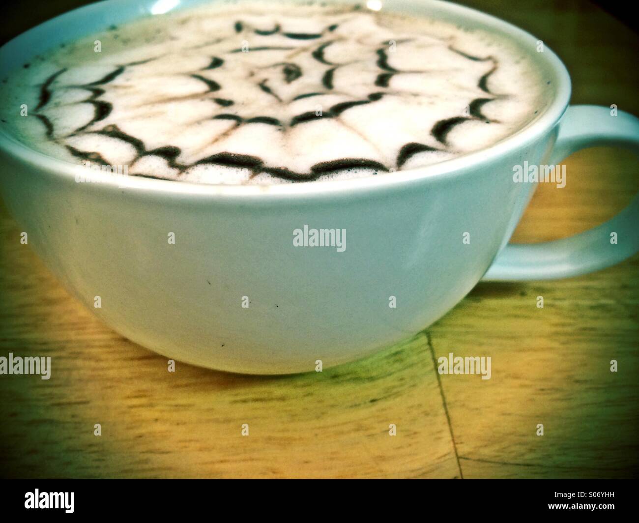 A latte coffee with a design drawn in chocolate syrup. - Smartphone Captured Stock Image