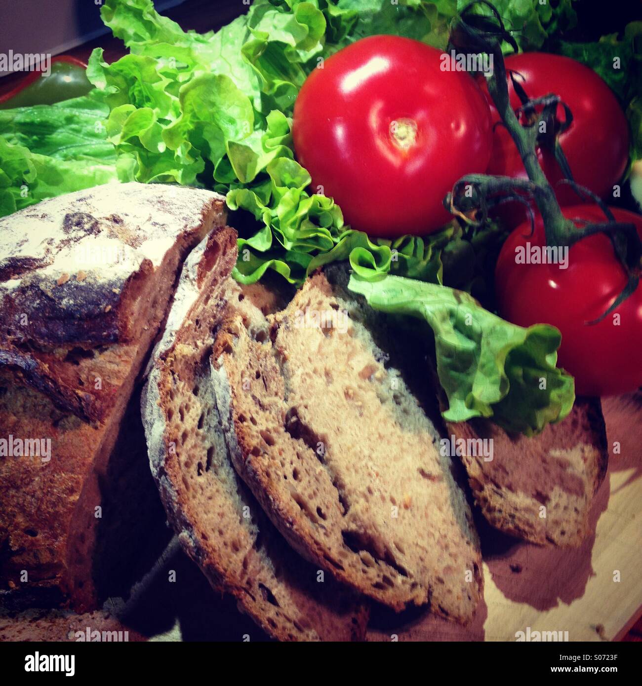 Rustic loaf of bread with green lettuce and red tomatoes. Mobile phone photo with some phone or tablet post processing. - Smartphone Captured Stock Image
