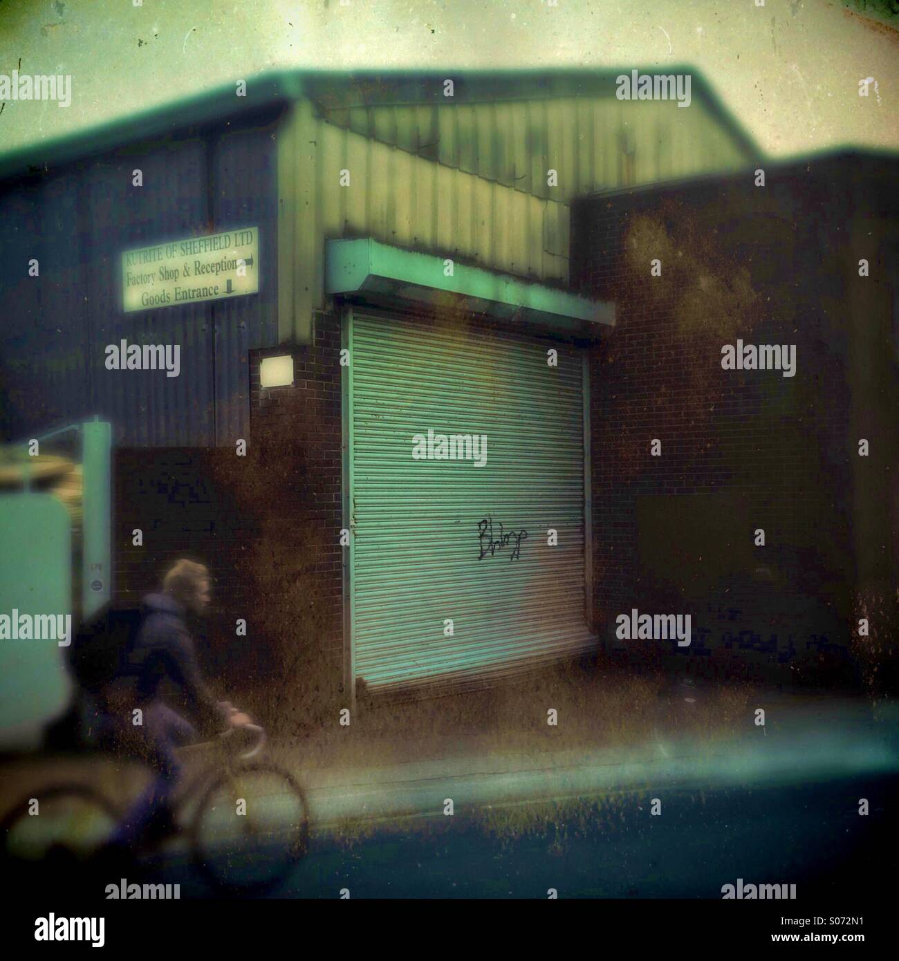 A man in a bike rides past a industrial unit - Smartphone Captured Stock Image