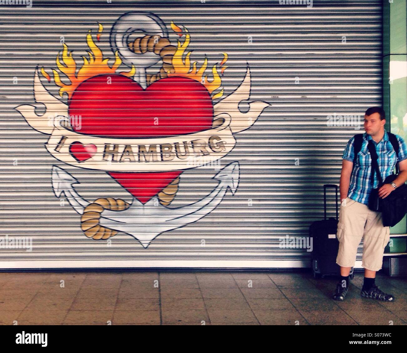 Man with luggage standing next to painted sign with 'I Love Hamburg' written inside of a heart in Altona train station, Hamburg, Germany Stock Photo