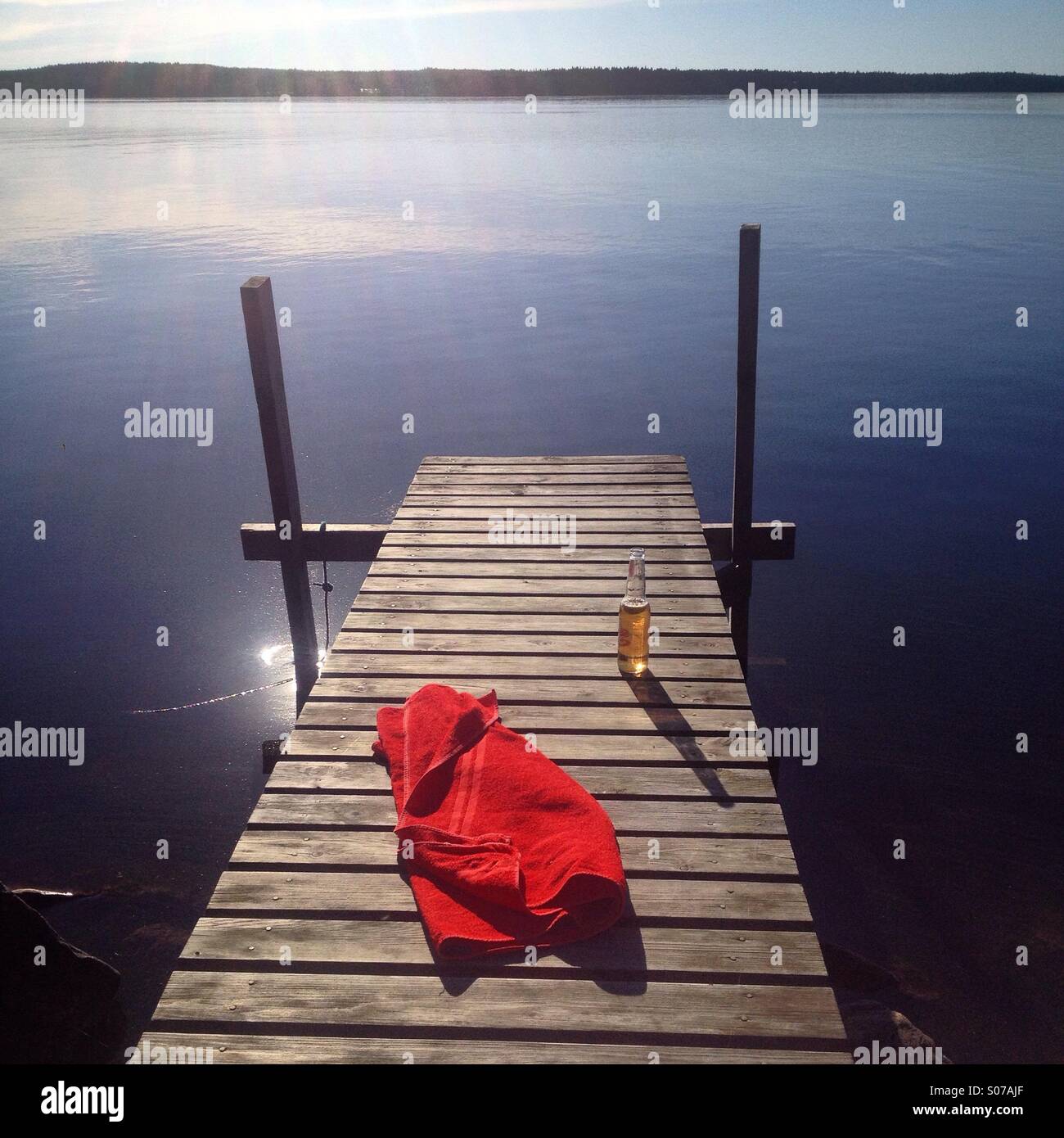 A cold beer and a towel on a jetty at an idyllic Nordic summerhouse lake in northern Finland Stock Photo