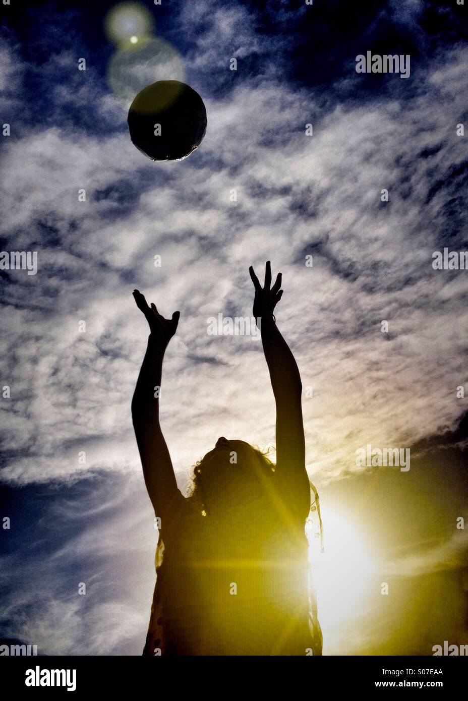 Young girl catching football backlit by sun Stock Photo