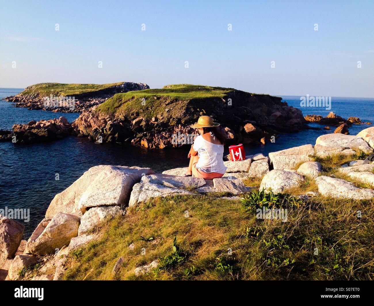 A woman sitting on a cliff in White Point, Nova Scotia. Stock Photo