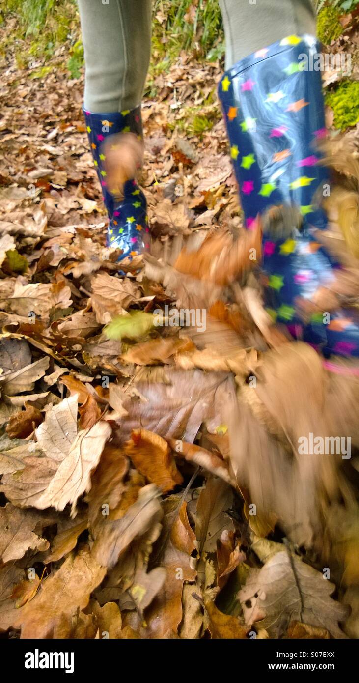 Autumn walk. Child in wellington boots kicking up autumn leaves on a footpath. Stock Photo