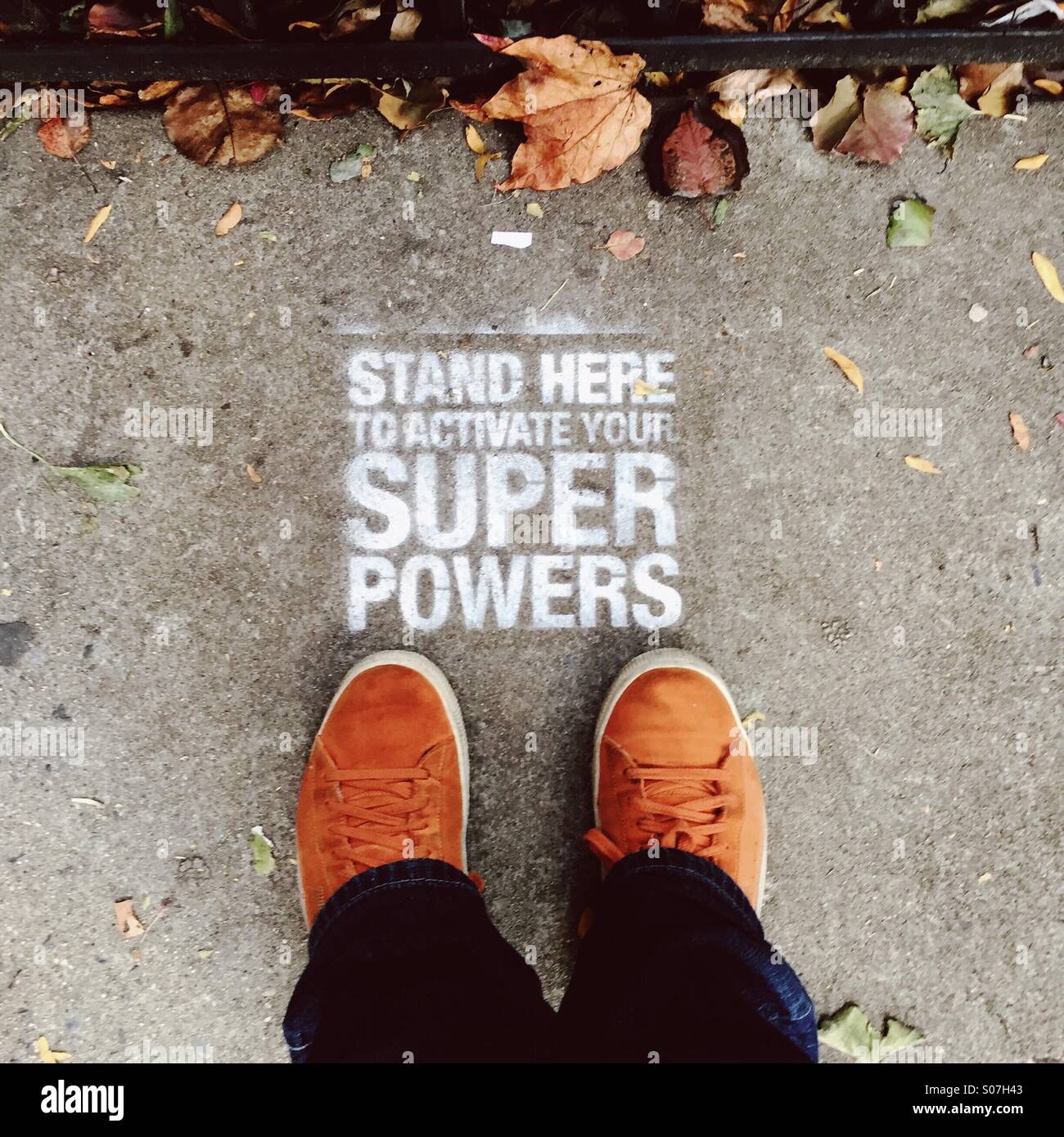 A person wearing orange shoes stands in front of stenciled graffiti that reads, 'stand here to activate your super powers' in the Chelsea neighborhood of New York City on Nov. 9, 2014. Stock Photo