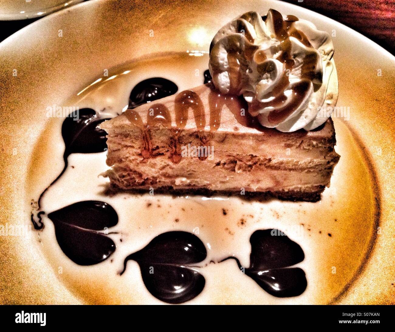 A slice of cheesecake with chocolate syrup hearts. - Smartphone Captured Stock Image