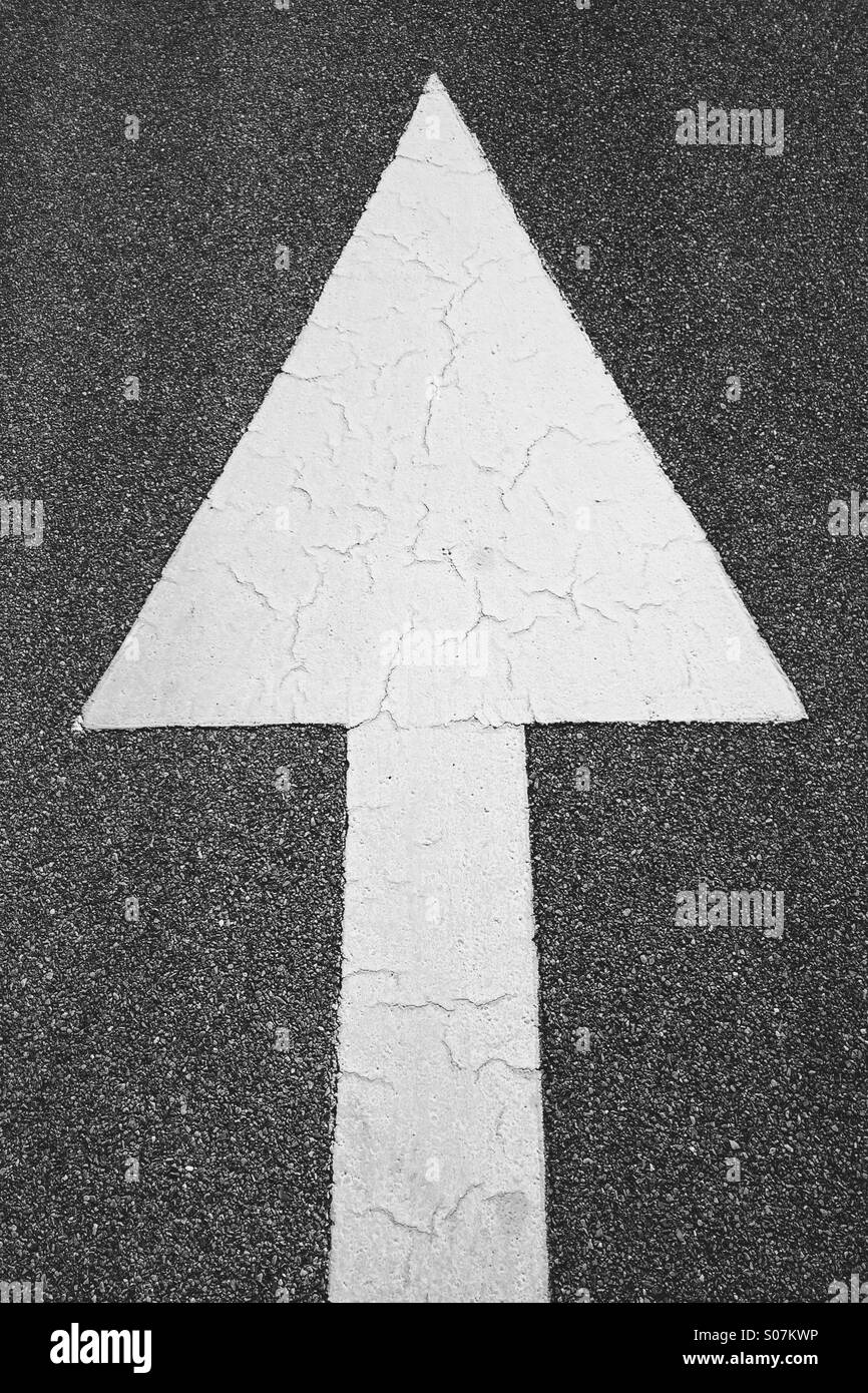 A bold painted white arrow on the road pointing up or ahead, in black and white . - Smartphone Captured Stock Image