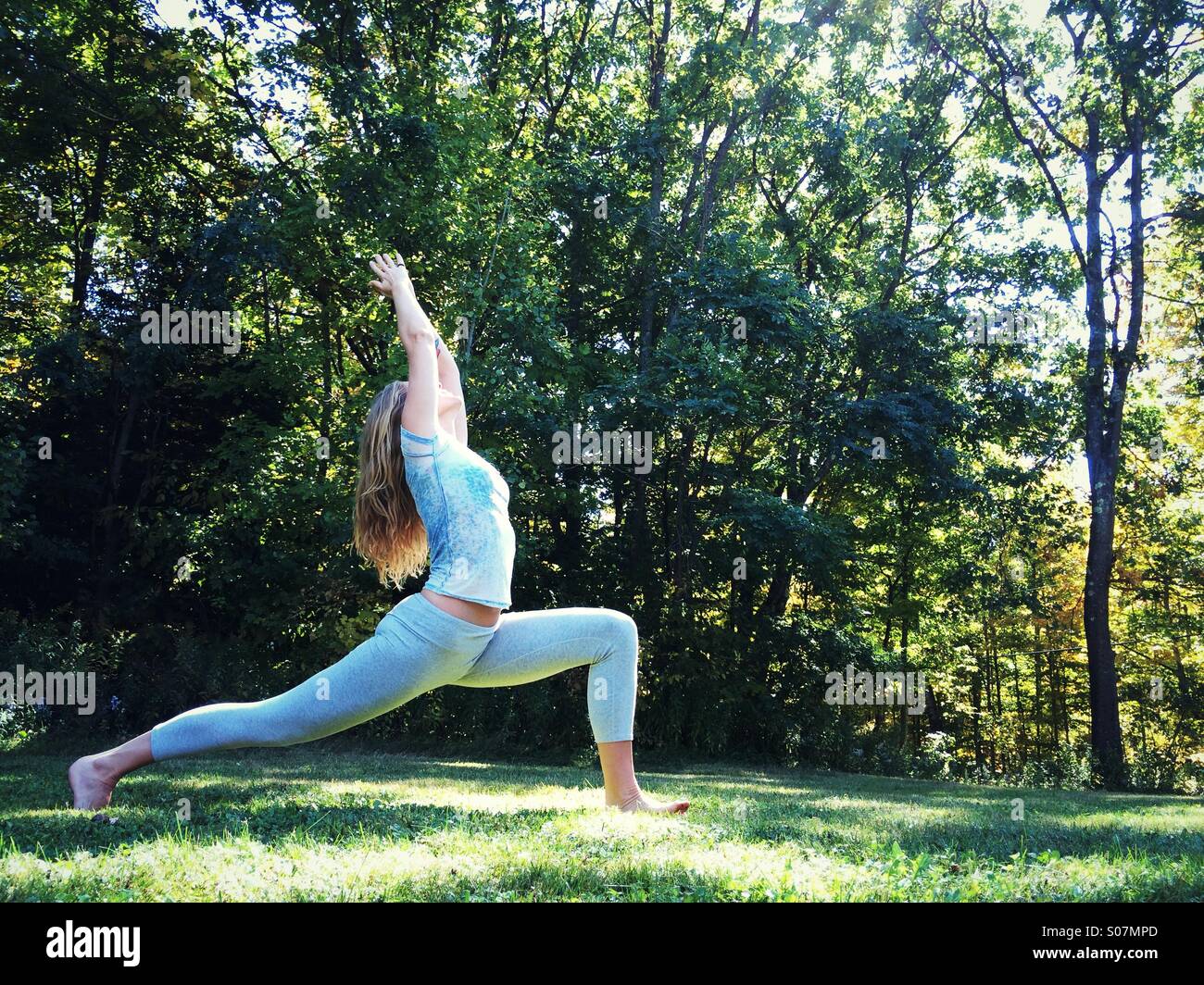 A woman doing yoga outside in the grass surrounded by nature. Stock Photo