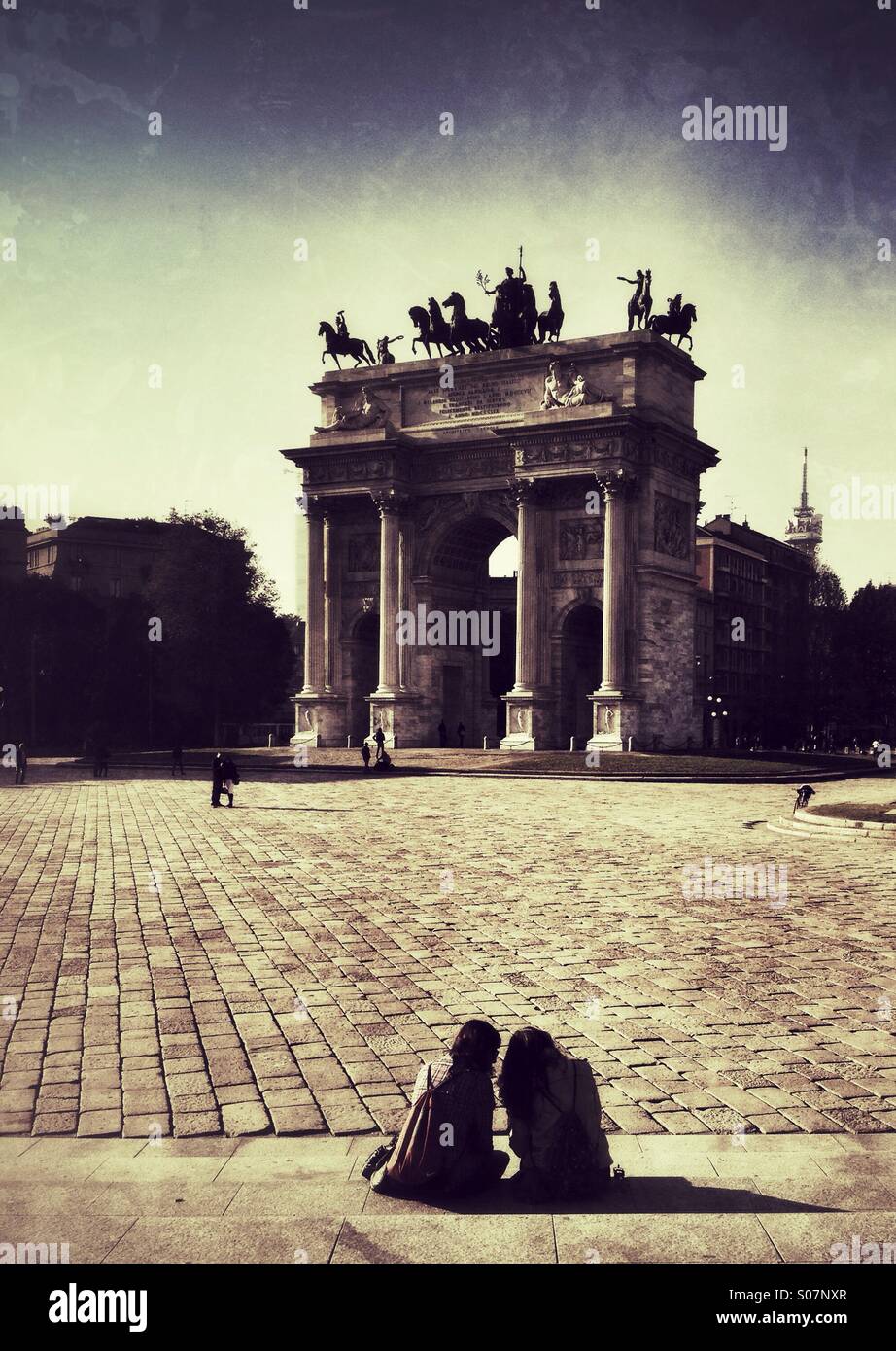 Two young women sit on some steps near the Porta Sempione in Milan, Italy - Smartphone Captured Stock Image
