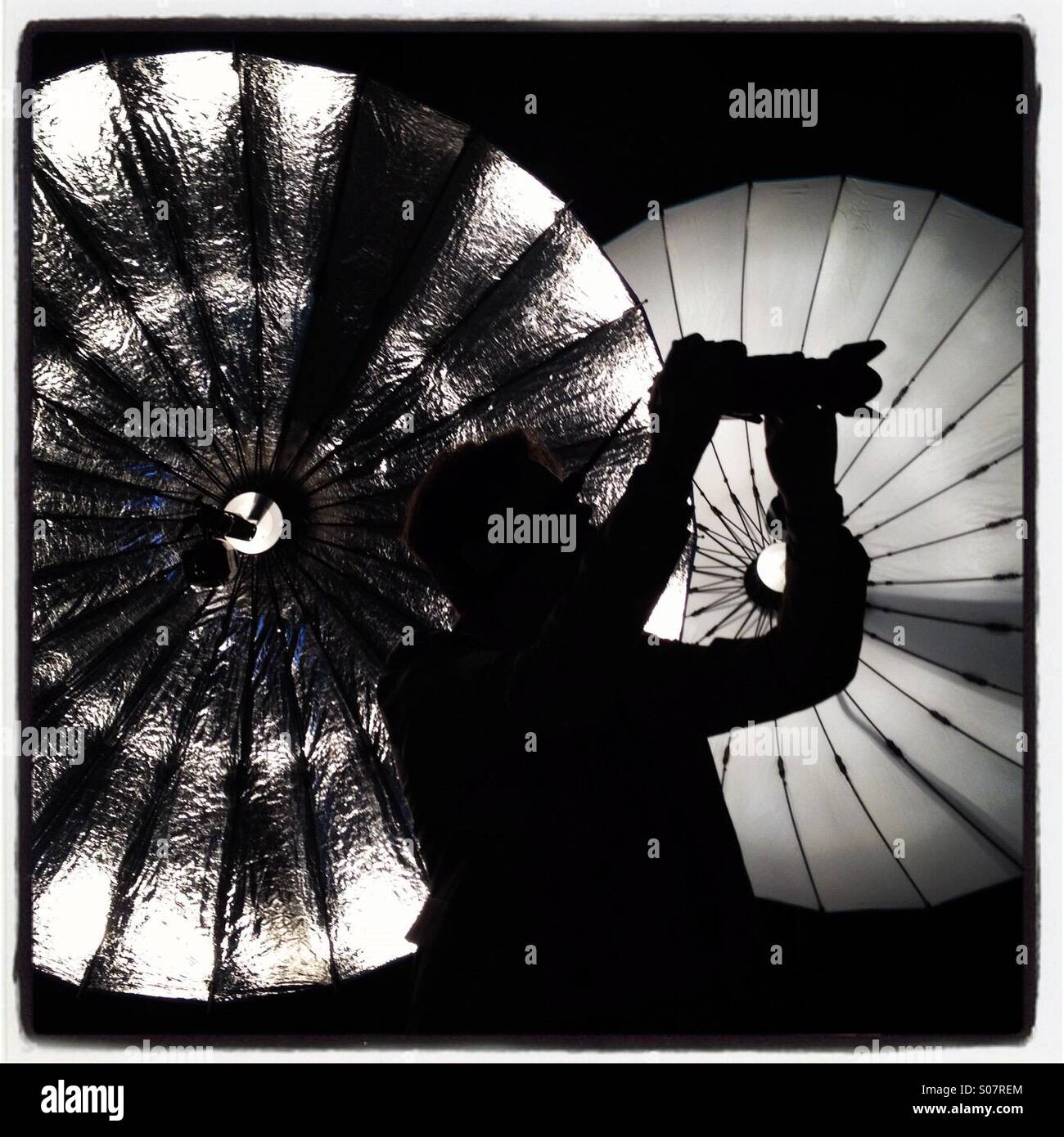 Photographer with medium format camera silhouetted in front of two parabolic umbrellas. - Smartphone Captured Stock Image