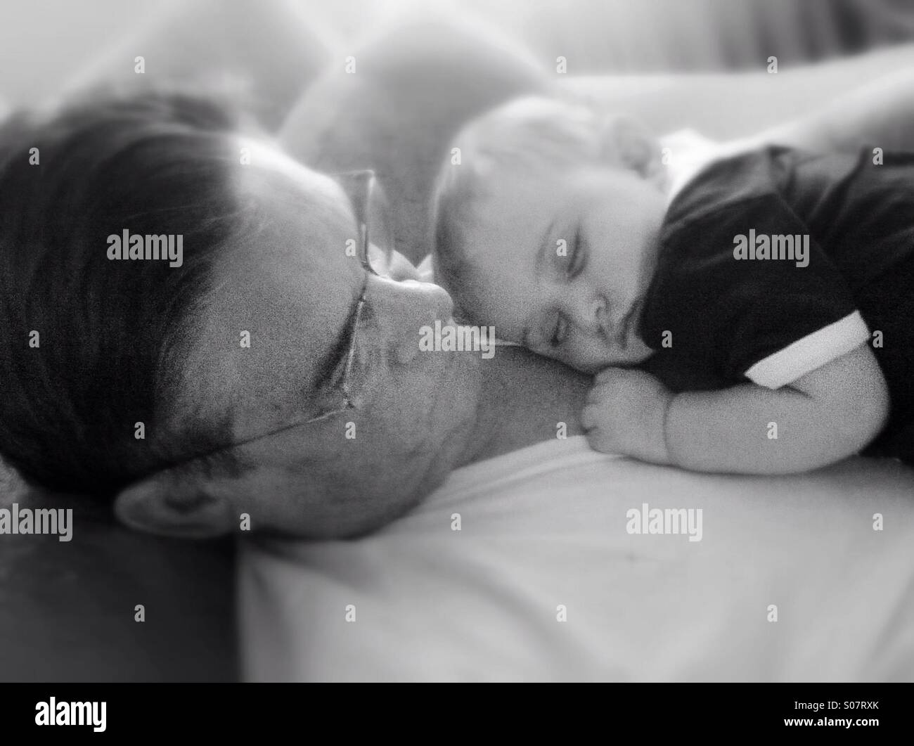 Soft image of granddad with baby boy sleeping on his chest. Black and