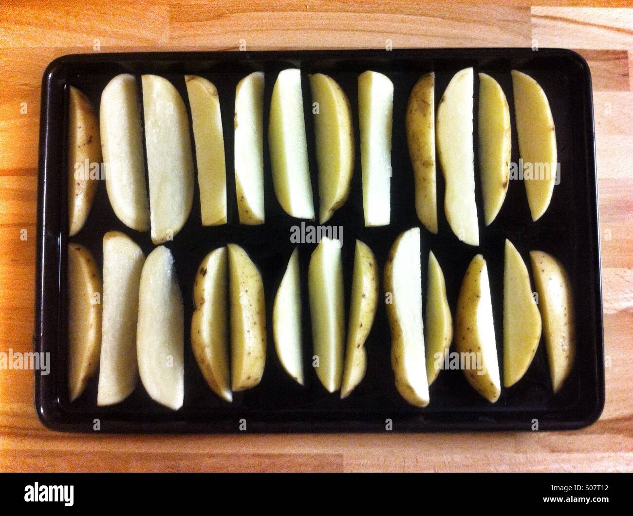 Crisp potato wedges arranged on a black tray ready for baking in a home kitchen setting at dinner time - Smartphone Captured Stock Image