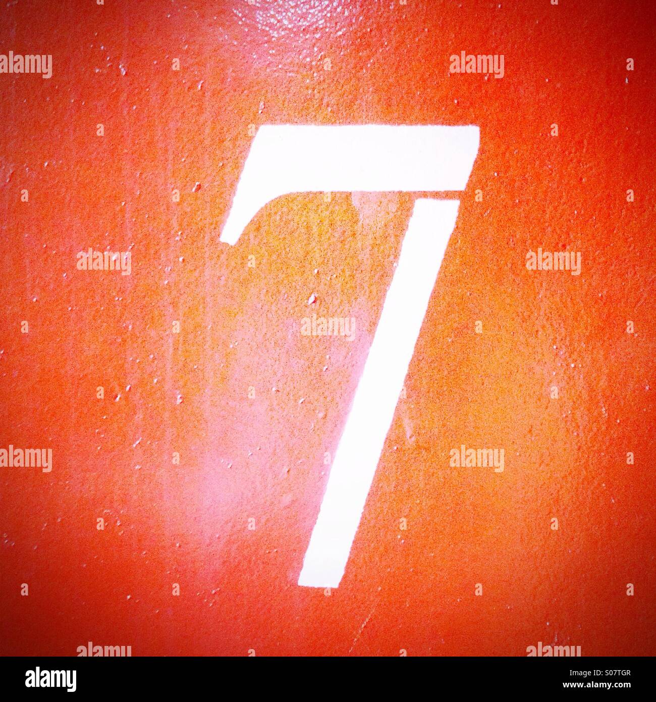 Number 7 painted in white on orange wall Stock Photo