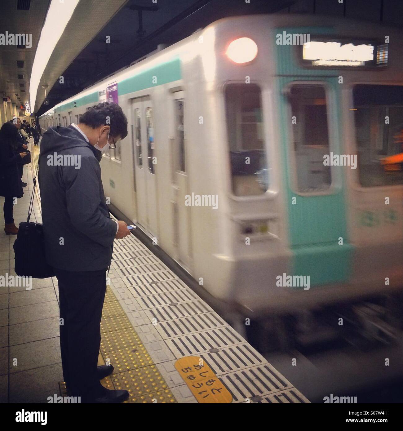 Man checks phone while waiting for subway, Kyoto, Japan - Smartphone Captured Stock Image