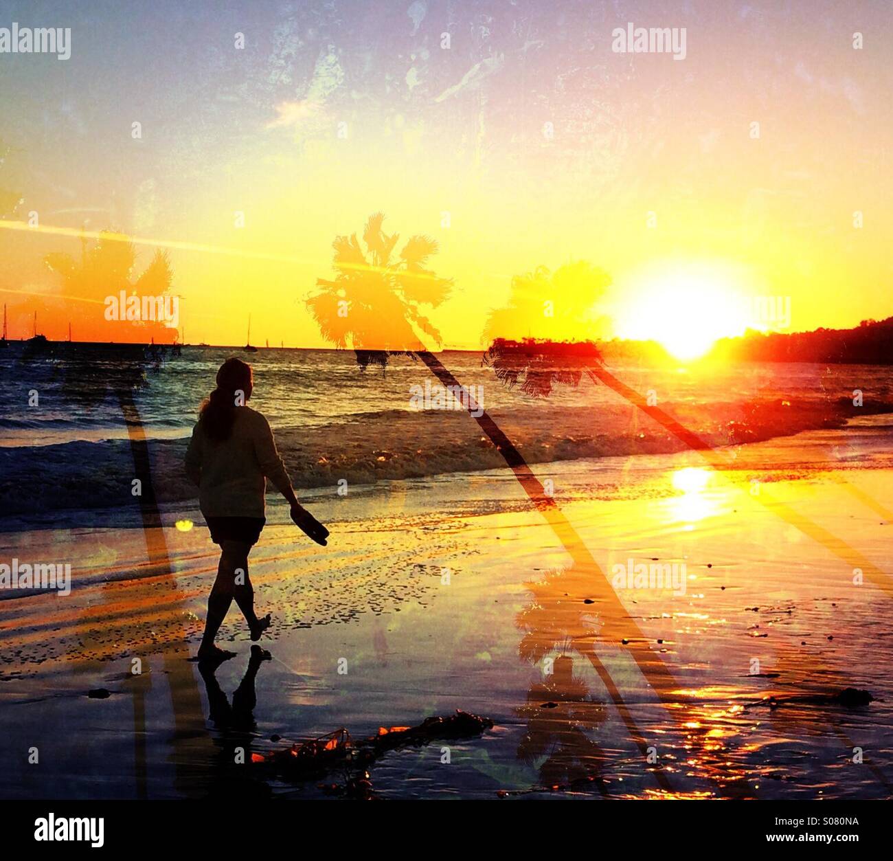 A woman walks along a beach in Santa Barbara, California at sunset. - Smartphone Captured Stock Image