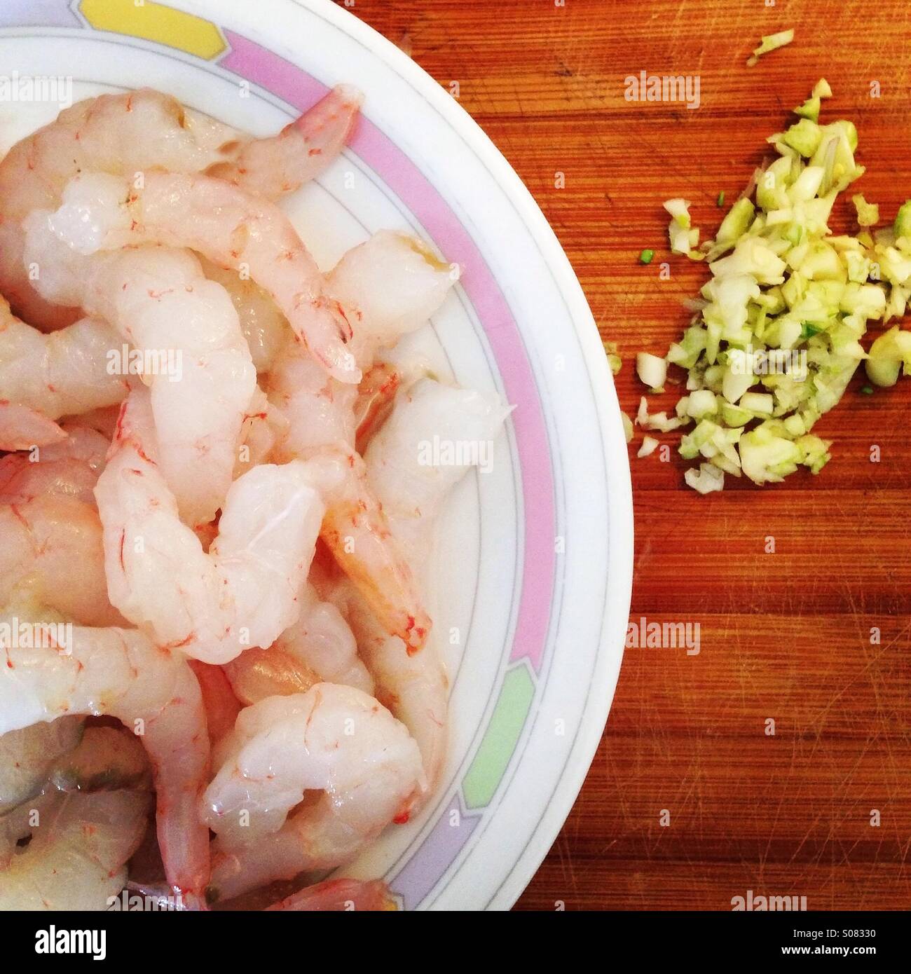 Prawns tails at plate with sliced garlic on wooden board Stock Photo