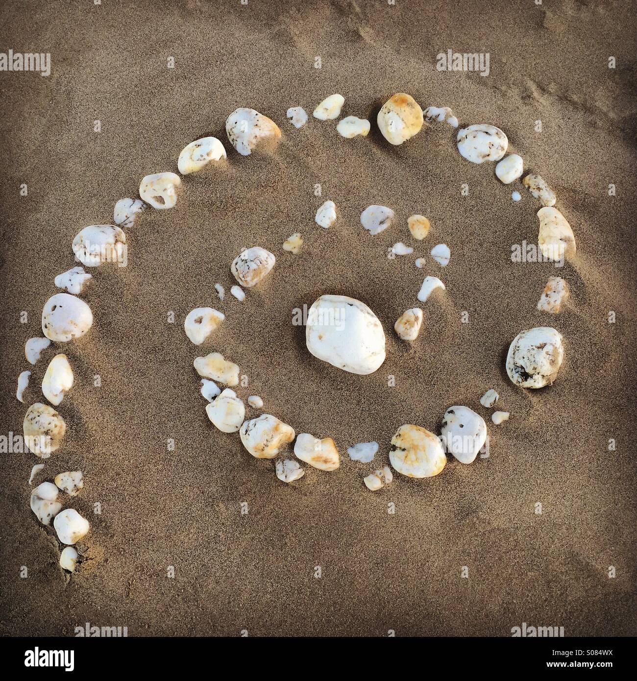 Beach art, spiral of pebbles on sandy beach Stock Photo