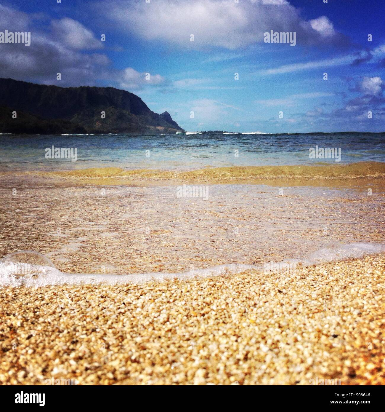 A view of sand, waves, Bali Hai, and Hanalei Bay from the beach at the St. Regis Kauai. Kauai Hawaii USA. Stock Photo