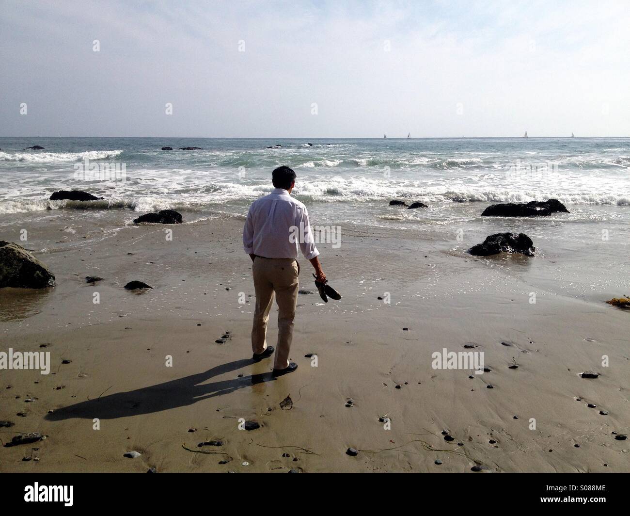 Business man on the beach with his shoes off walking to the ocean. Stock Photo