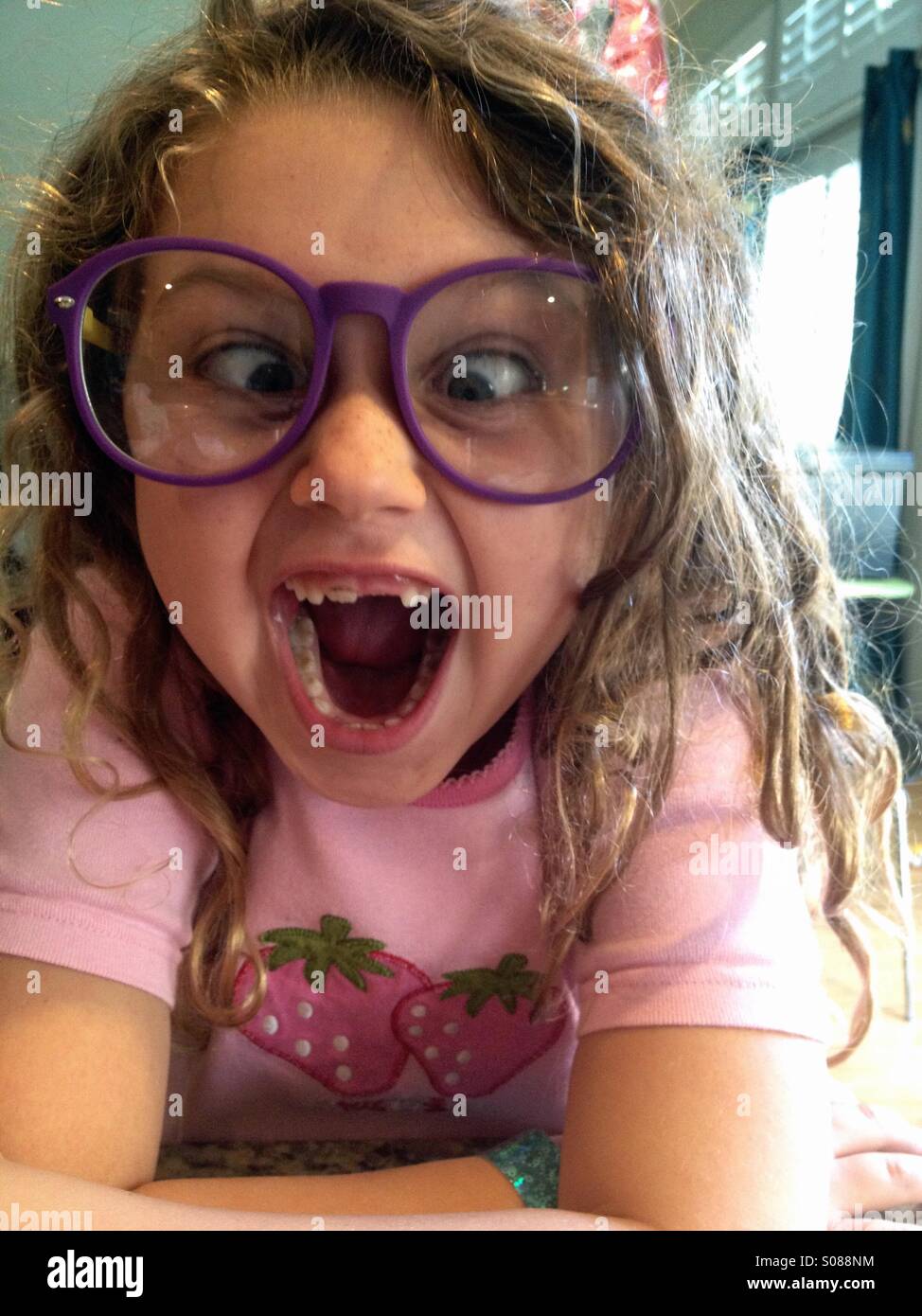 Young girl wearing big glasses and front teeth missing and playing cross eyed. Stock Photo