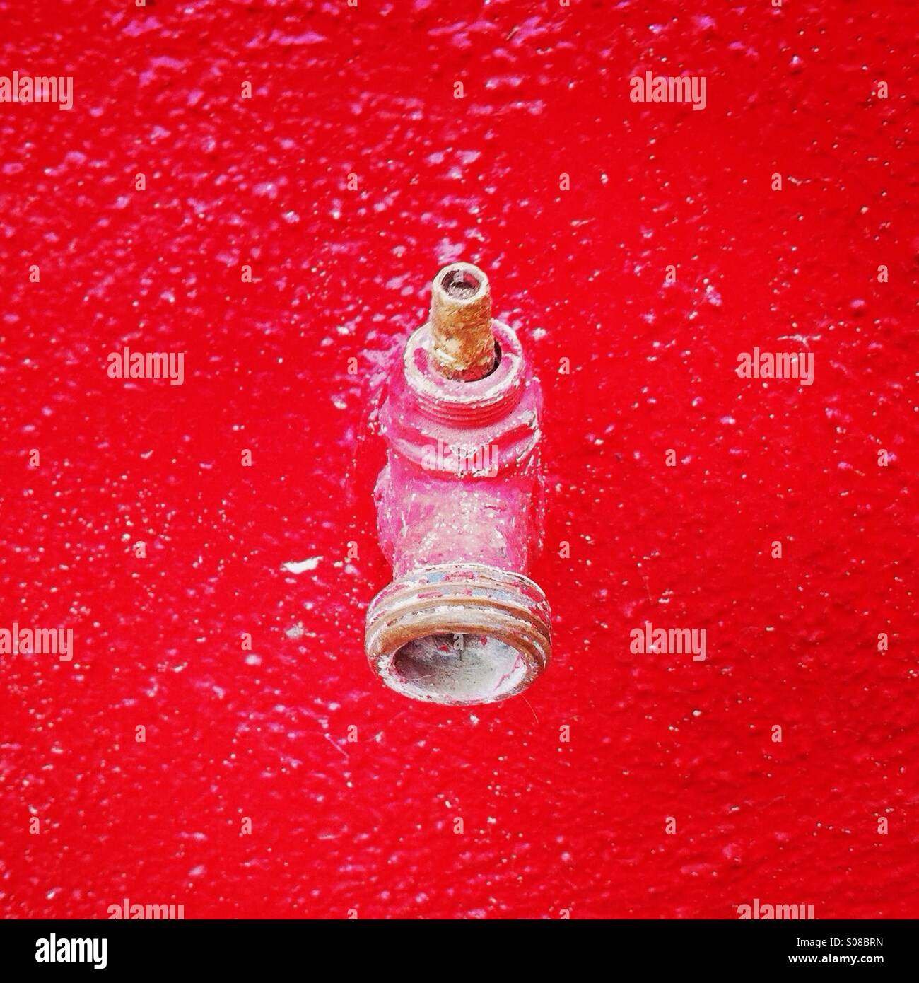 A dried up water faucet on a red wall. Stock Photo