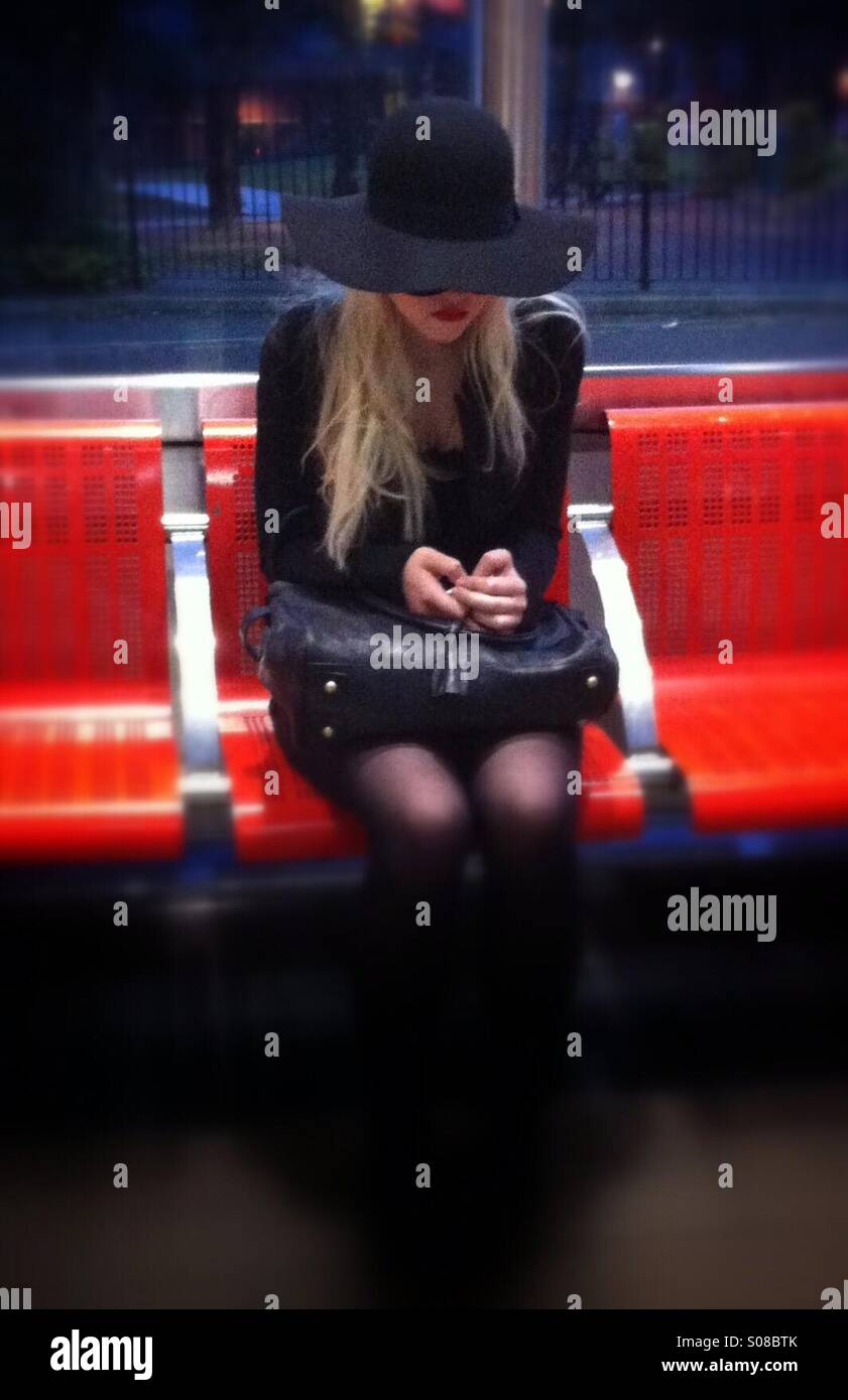 A young female checks her phone while waiting in Walthamstow Bus Station - Smartphone Captured Stock Image