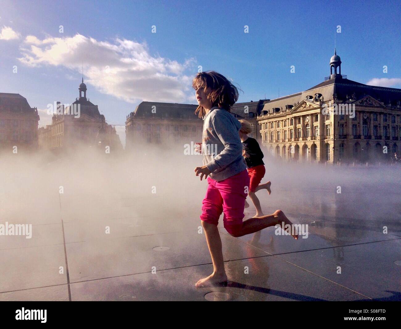 A group of children playing with water in Place de la Bourse in Bordeaux - Smartphone Captured Stock Image