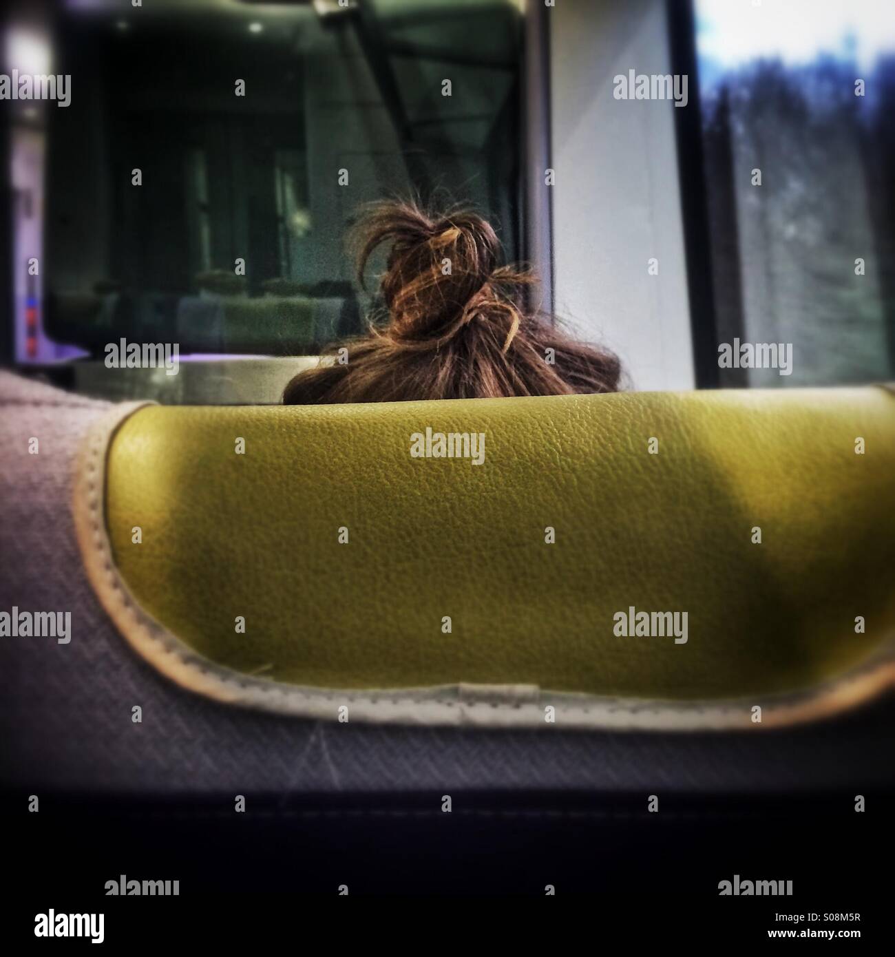 A woman with a loose bun hairstyle seen from the back of a train seat - Smartphone Captured Stock Image