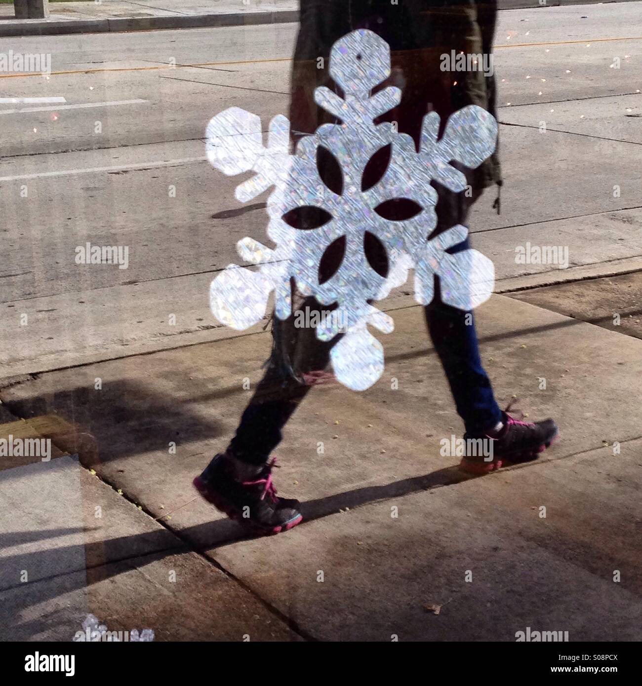 Pedestrian's reflection in a white paper snowflake decorated window, sidewalk scene Stock Photo