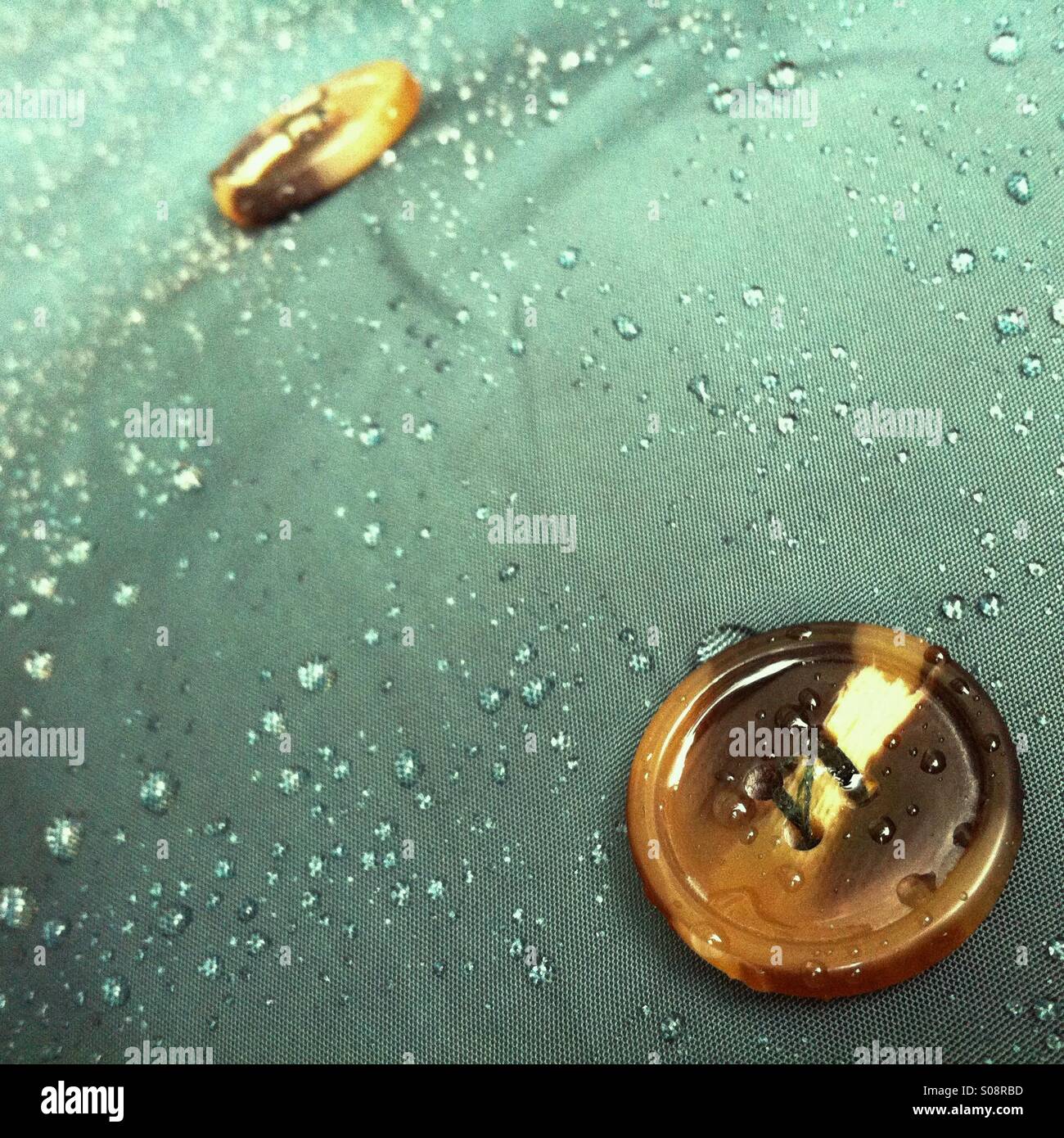 Closeup of water droplets and buttons on a dark green mackintosh Stock Photo