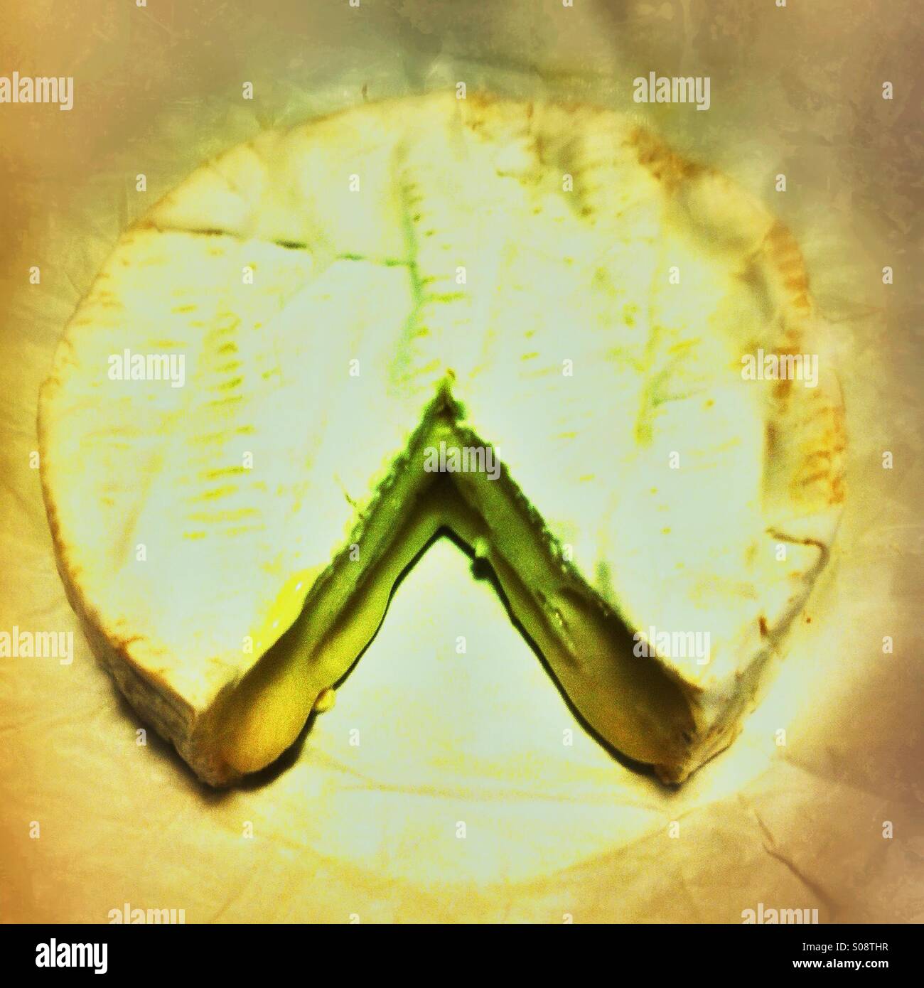 A round Camembert cheese with a smooth exterior displays a wedge cut out. The cheese is presented on a rustic wooden board, ideal for sharing. - Smartphone Captured Stock Image