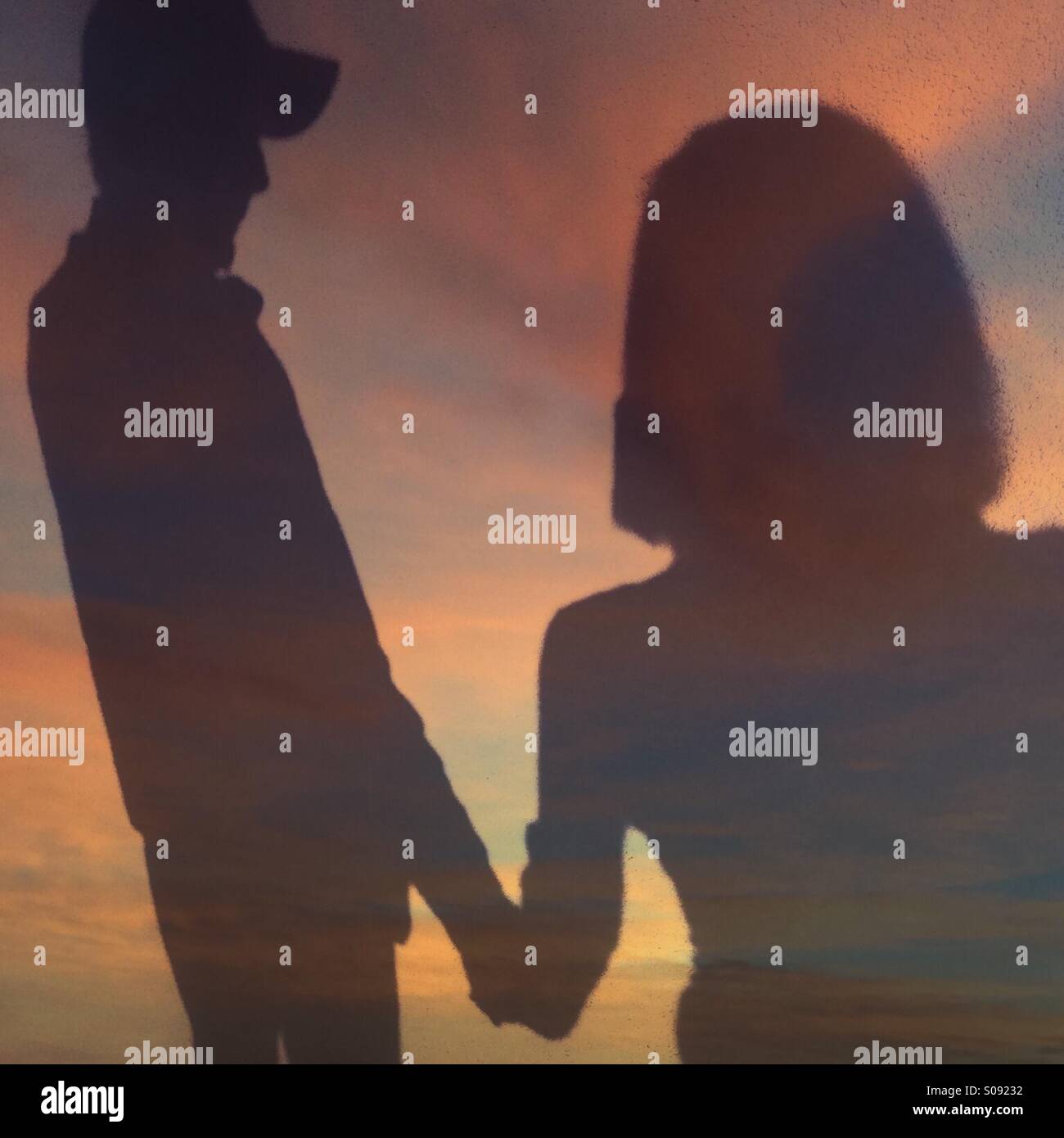 Double exposure of a man and woman holding hands blended with a photo of a sunset at the beach - Smartphone Captured Stock Image