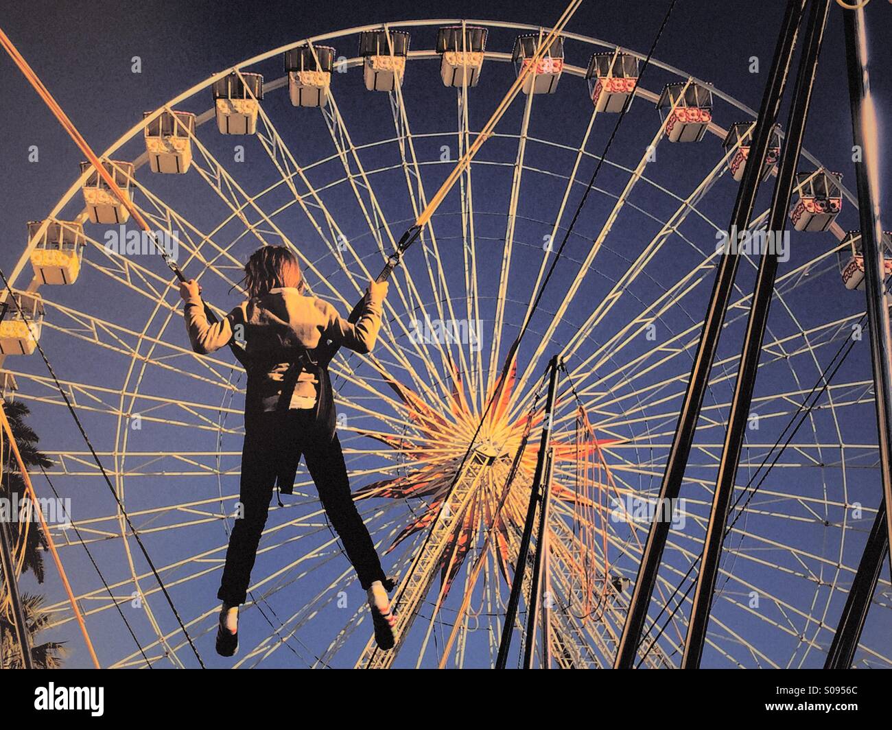 Child playing on a bungee rope in front of a Ferris wheel - Smartphone Captured Stock Image