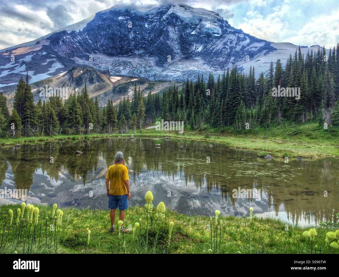 Hiker standing next to small pond reflecting Mount Rainier along the Wonderland Trail in Mount Rainier National Park. Stock Photo