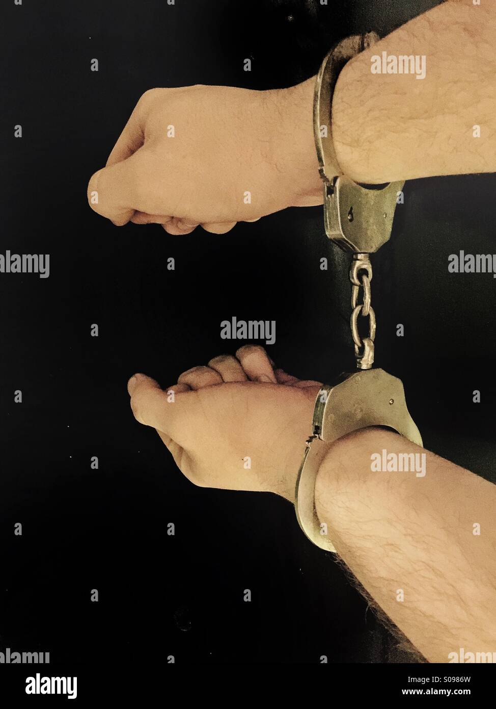 Pair of hands being restrained with police handcuffs Stock Photo