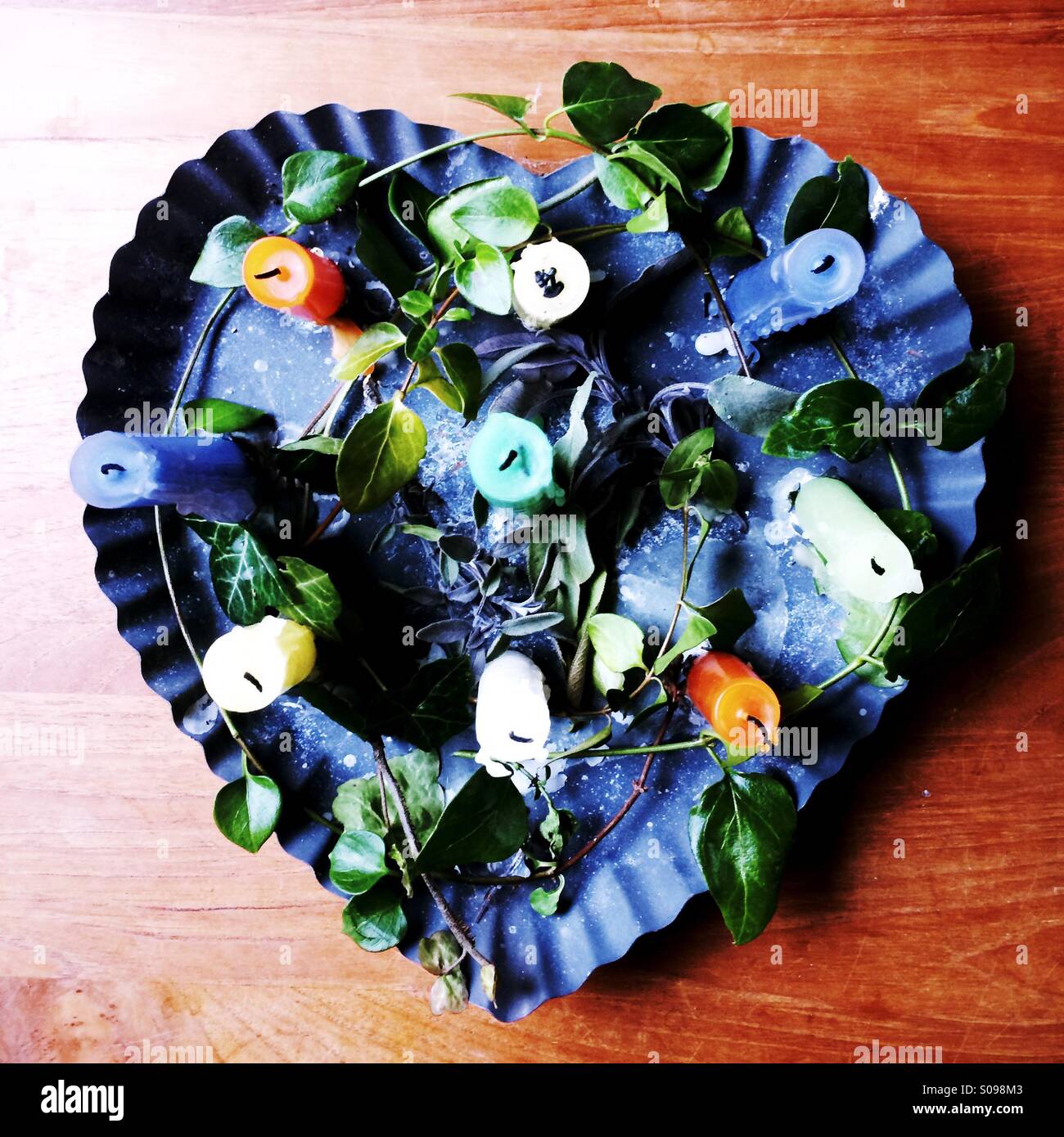 A heart shaped metal candle holder filled with multicolored candles and greenery makes a beautiful centerpiece. - Smartphone Captured Stock Image