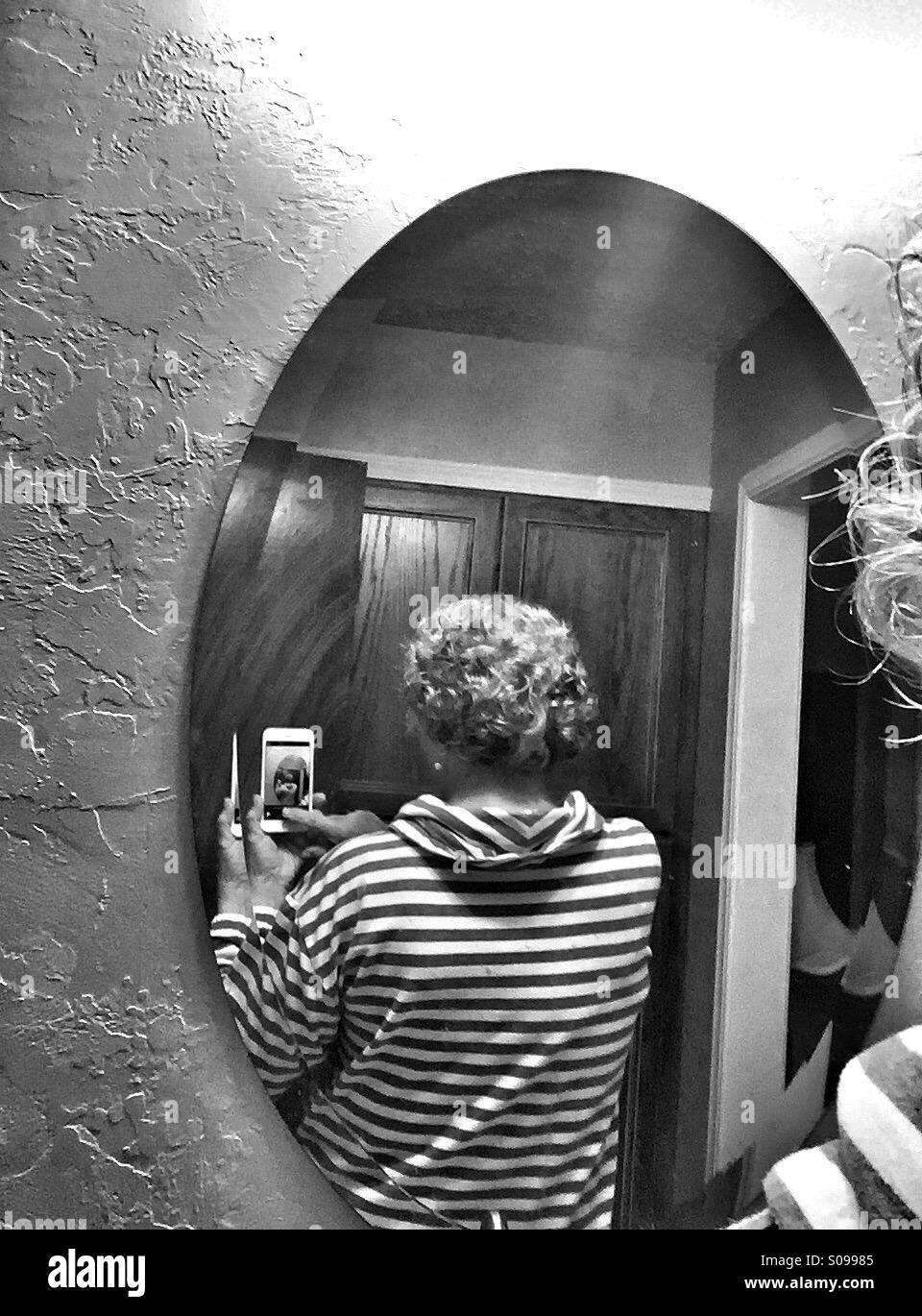 An older Caucasian woman takes a cell phone photo of the back of her hair using a mirror. - Smartphone Captured Stock Image