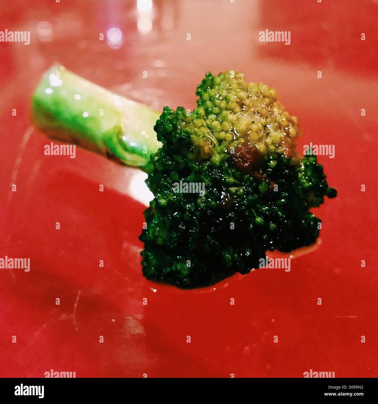 A piece of broccoli sits in a bright red sauce. Stock Photo